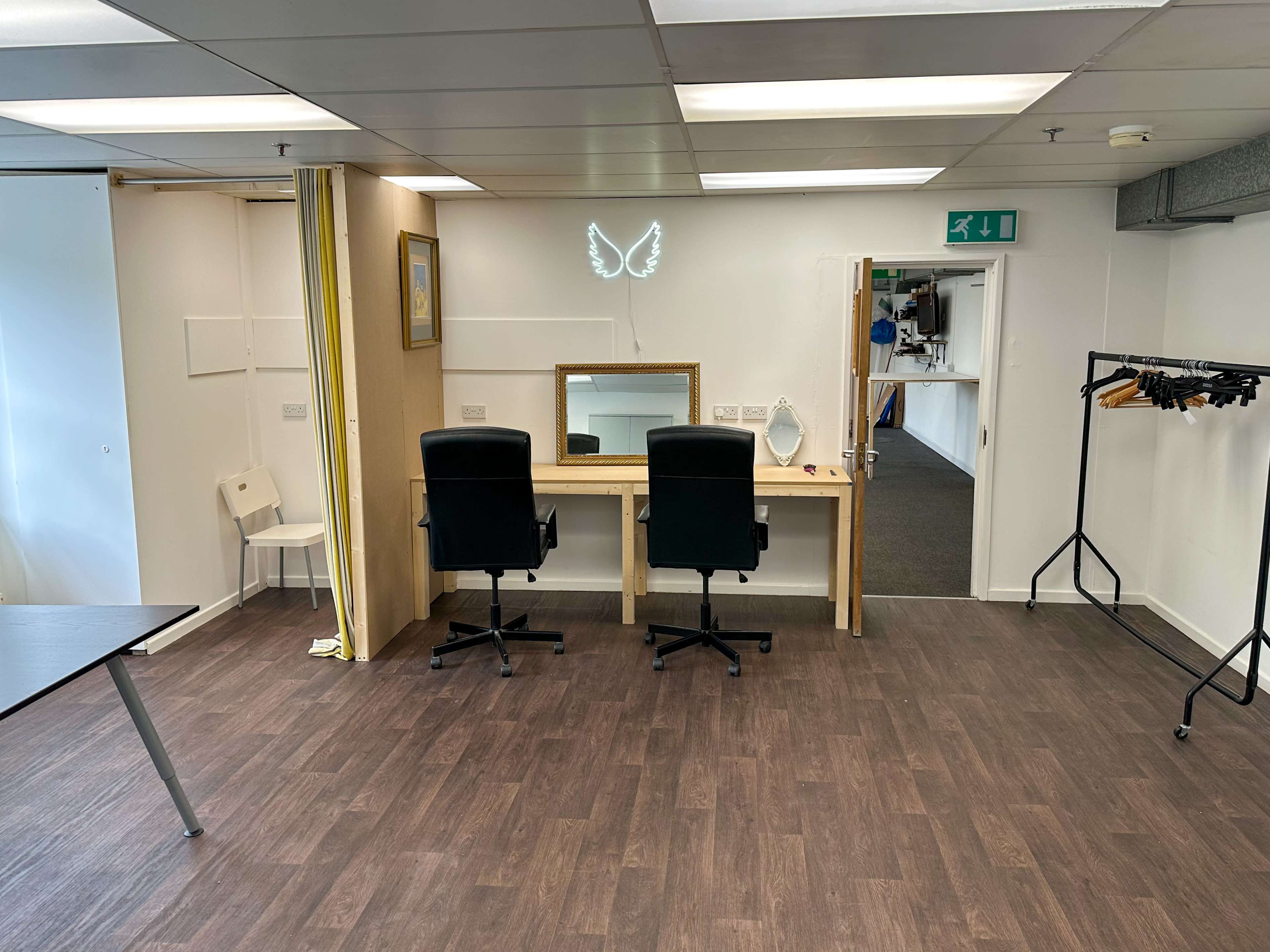 A simple room with two office chairs facing a mirrored desk, flanked by a folding screen and a clothing rack on the side.