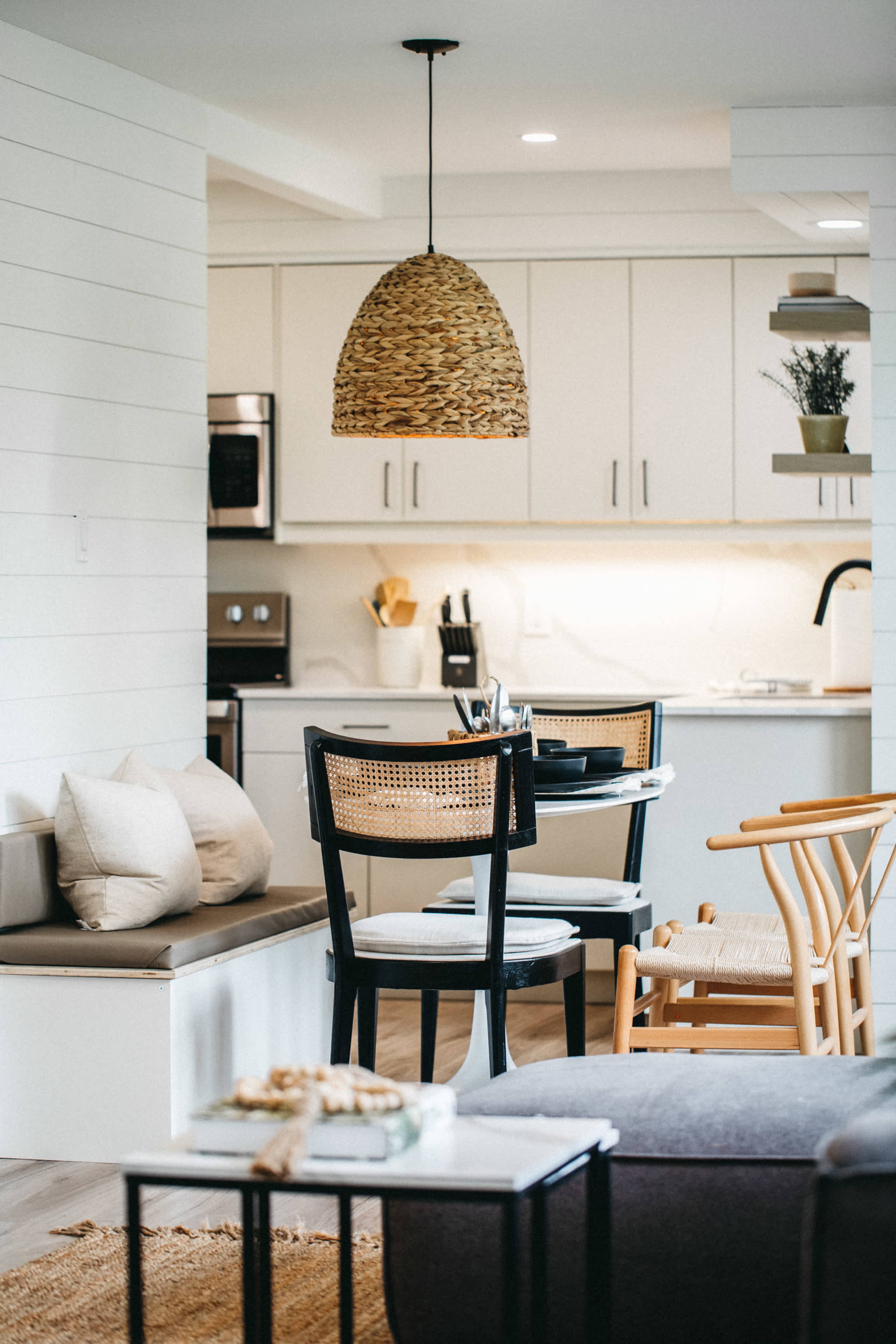 A modern kitchen and dining area features a woven pendant light, a wooden dining table with chairs, and minimalist decor.