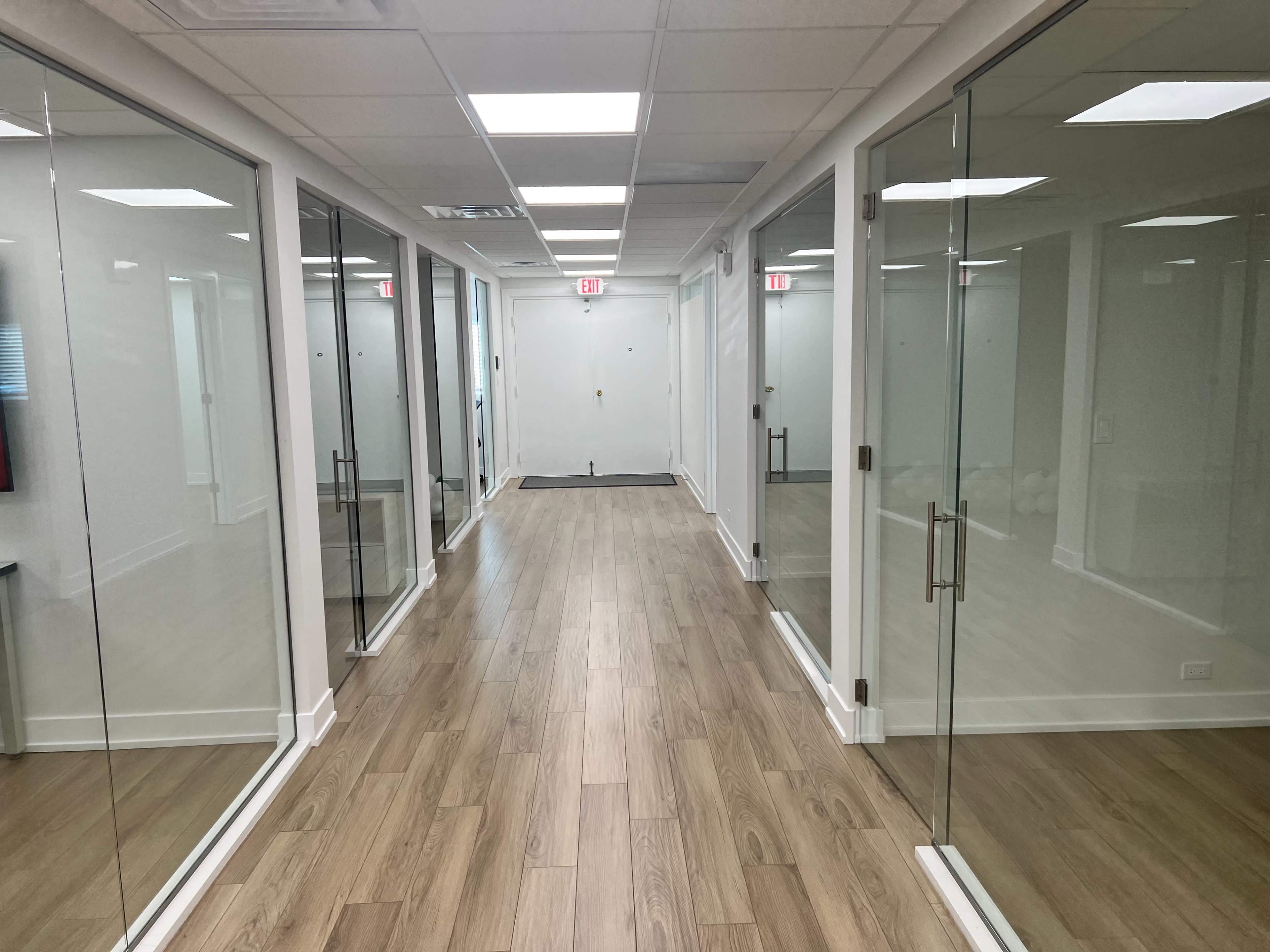 A hallway features glass-walled offices on both sides and a wooden floor.
