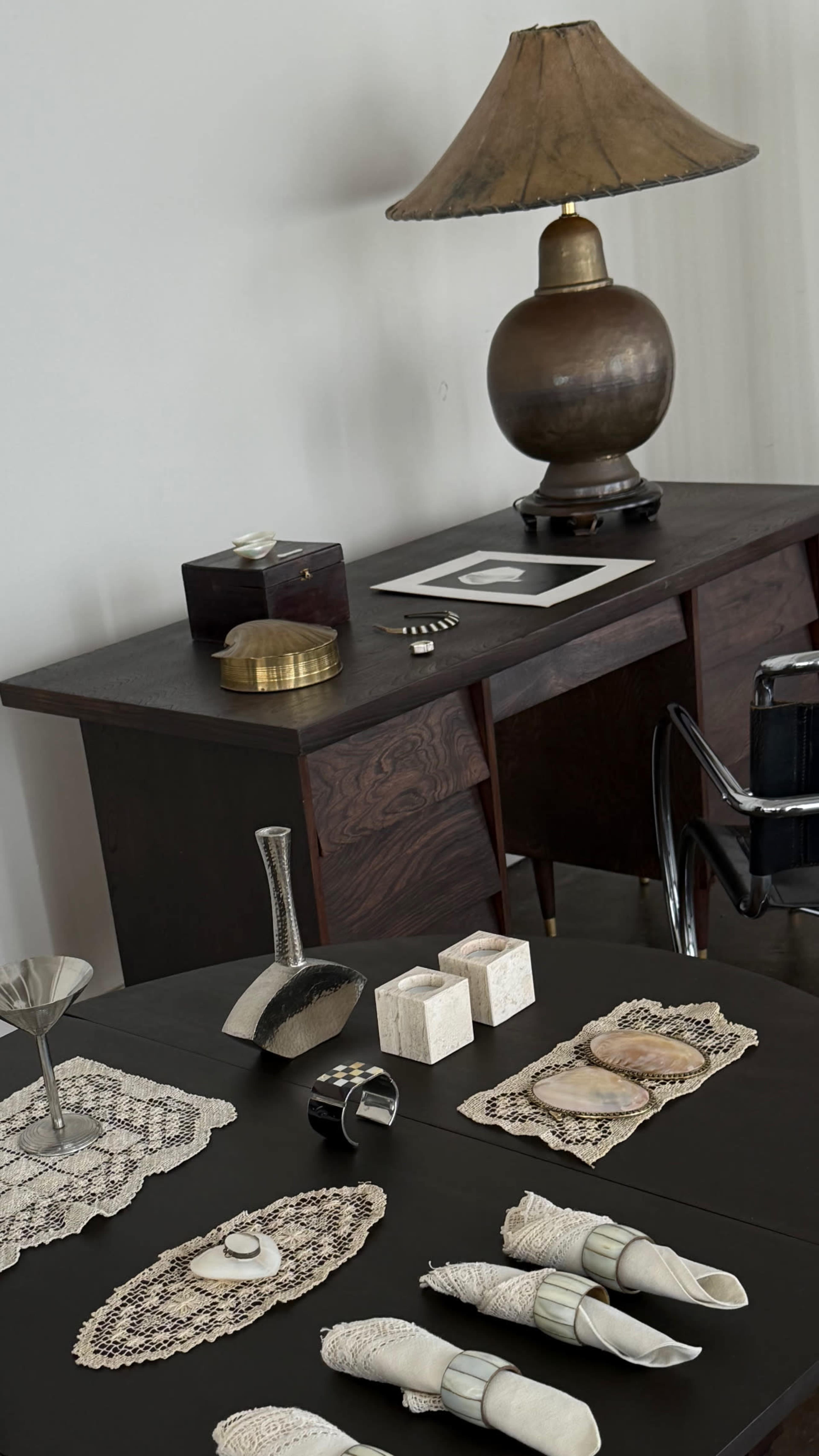 A wooden desk with various decorative items, including a lamp, a box, and metallic accents, is displayed against a plain wall.