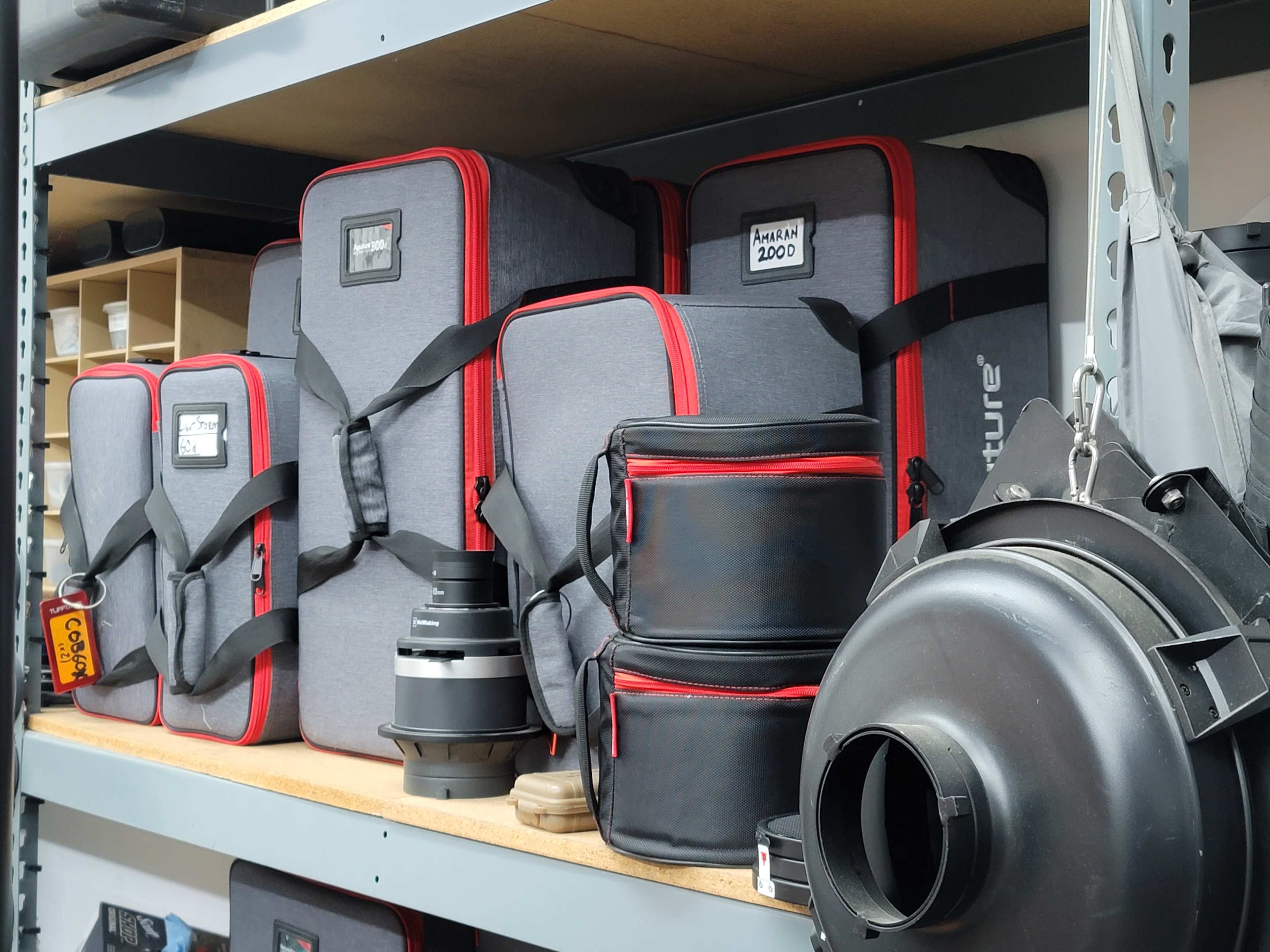The image shows a shelf filled with camera bags and equipment, including lens cases and a large camera accessory.