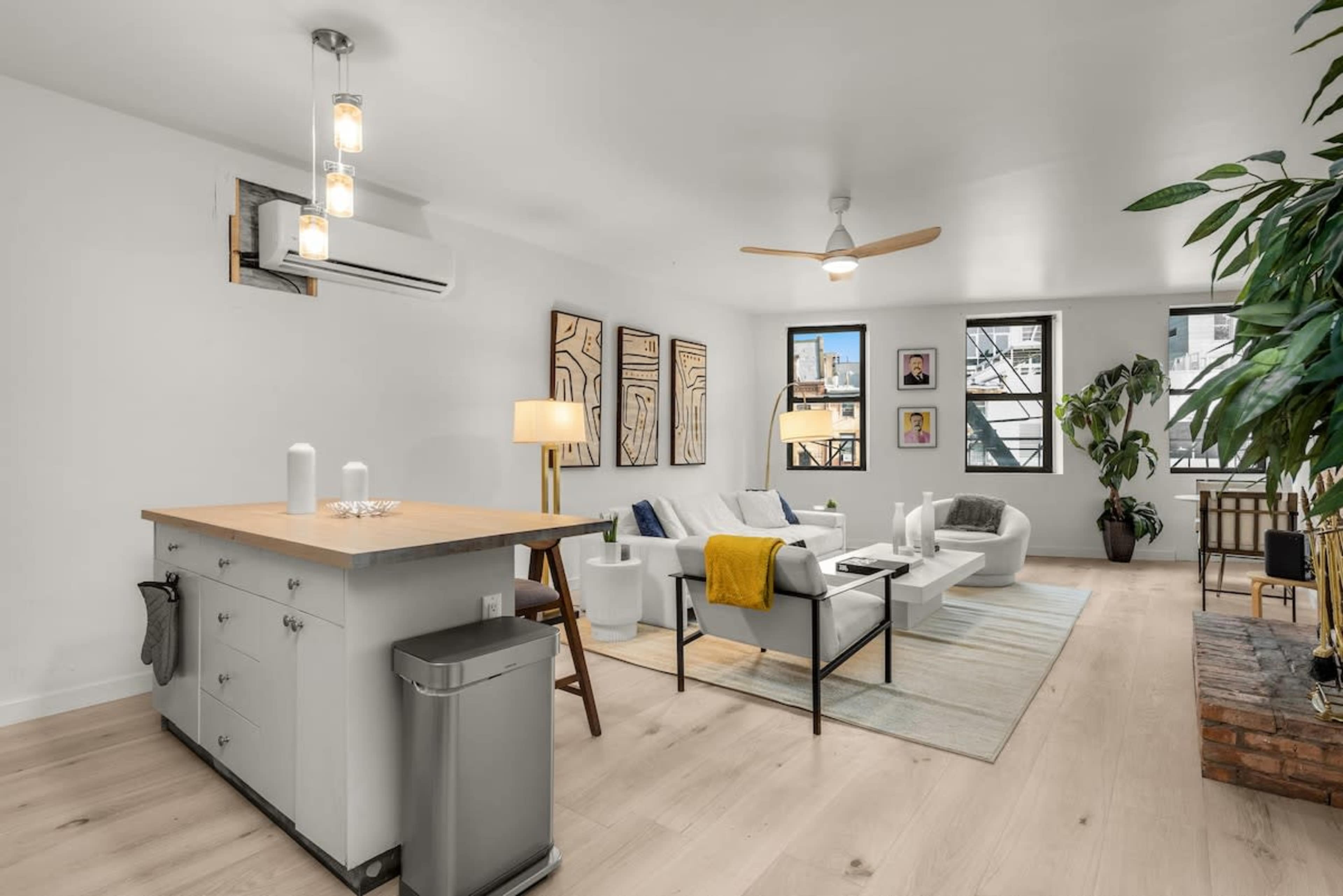 A modern living room with light wood flooring, a minimalist kitchen island, and comfortable seating arranged around a coffee table.
