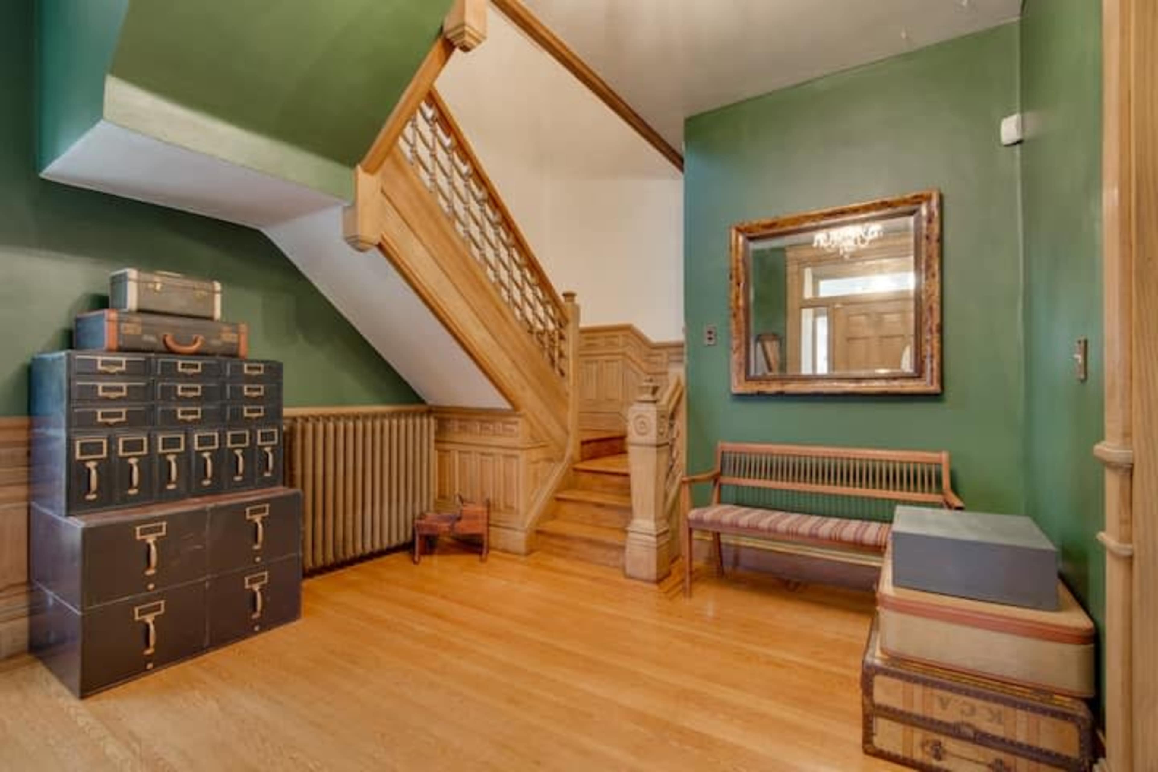 The entryway features a staircase, a wooden bench, and a storage chest against green walls.