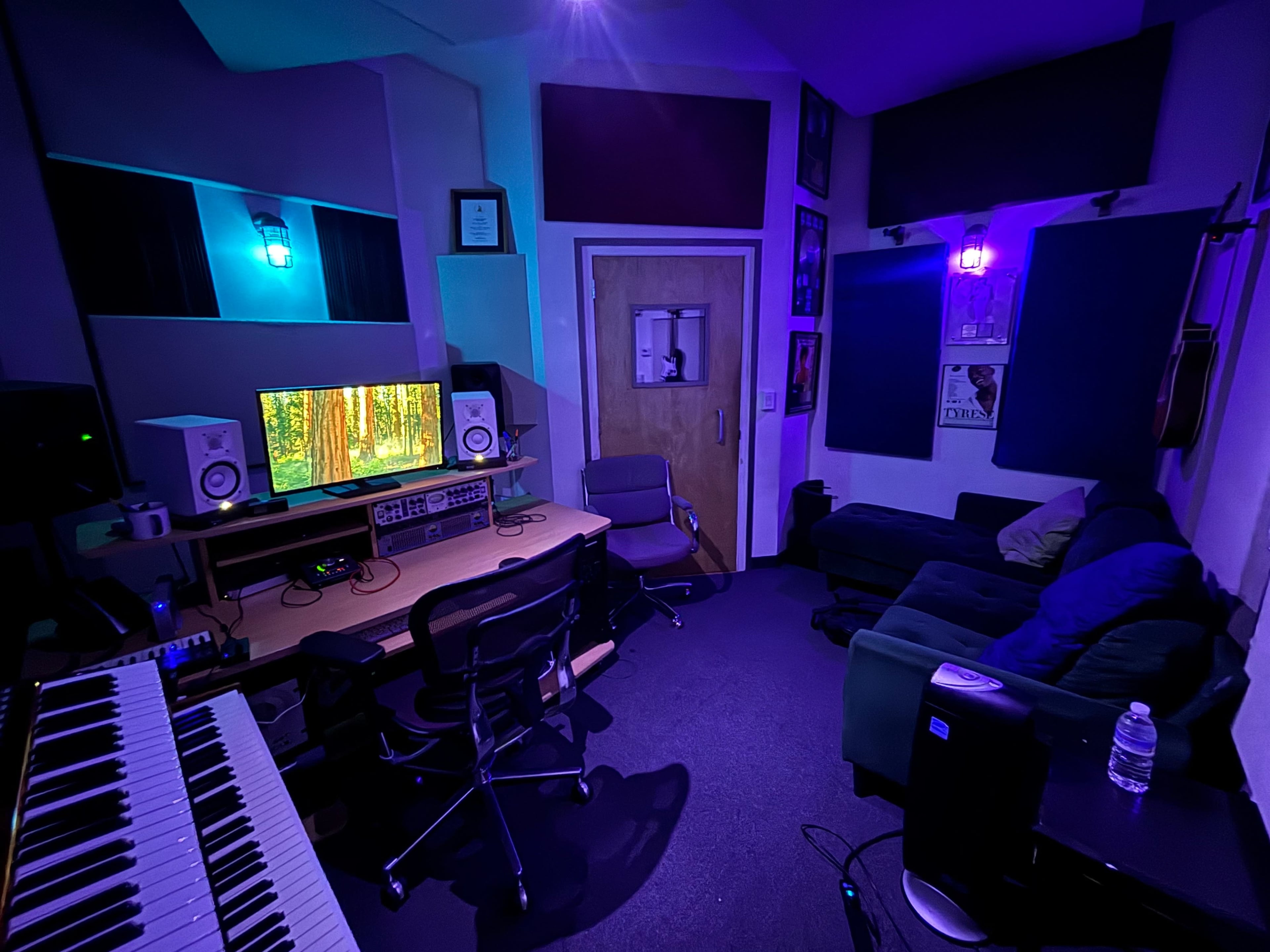 The image shows a recording studio with a desk featuring computer monitors, a keyboard, and a cozy seating area with a green couch.