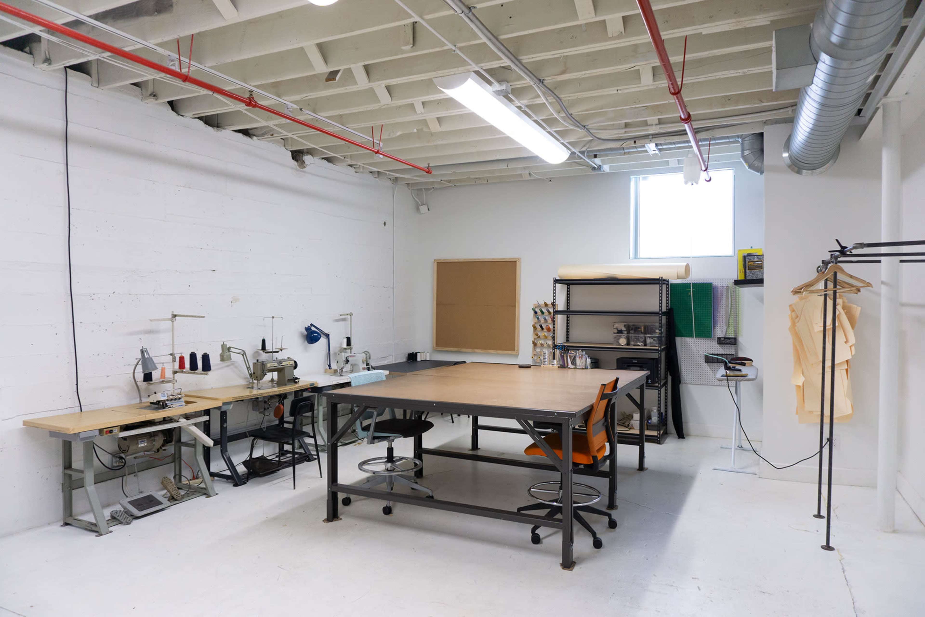 A spacious workshop with sewing machines, a large table, and various materials arranged around the room.
