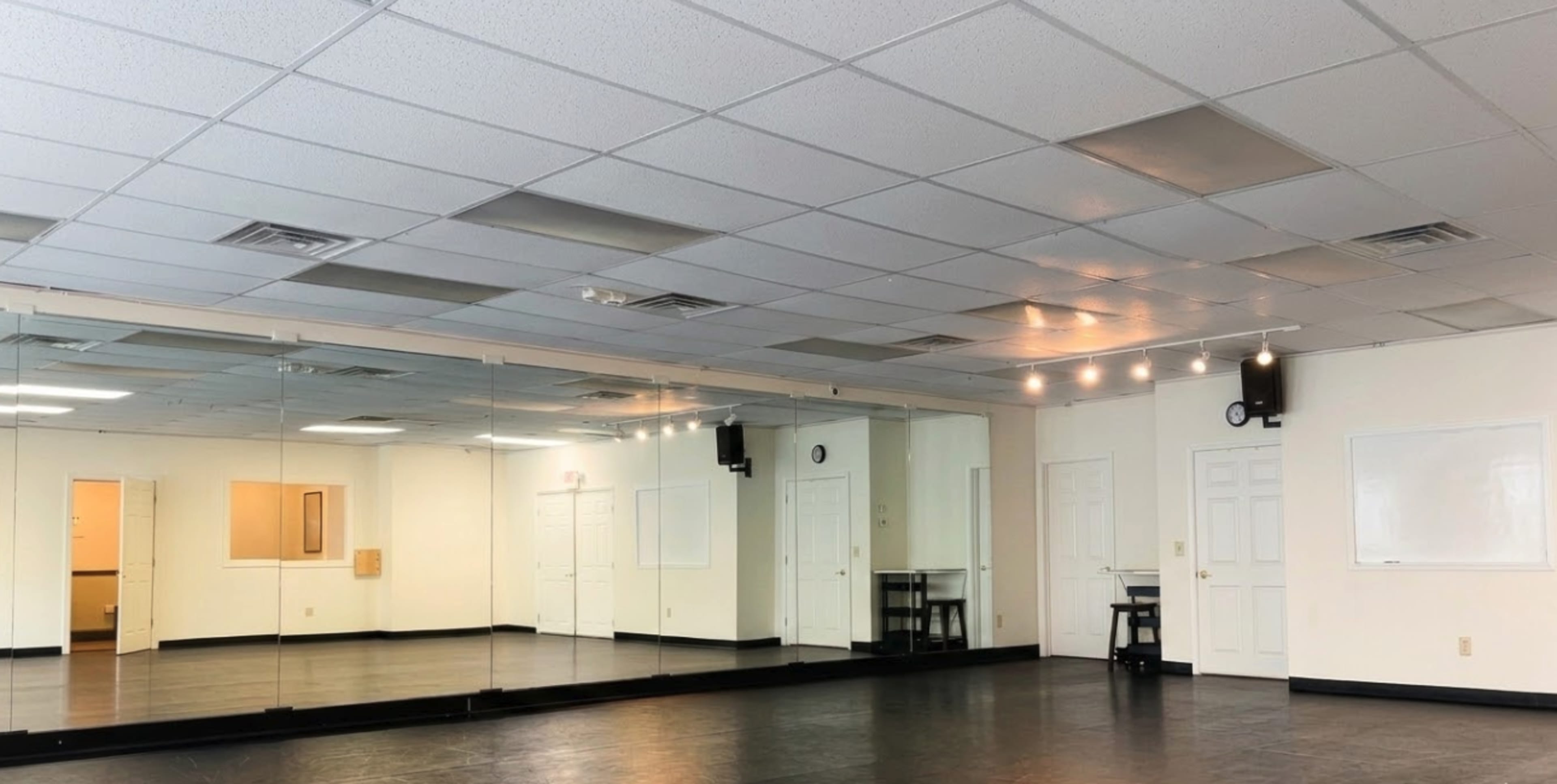 The image shows a dance studio with mirrored walls, a black floor, and a few light fixtures on the ceiling.