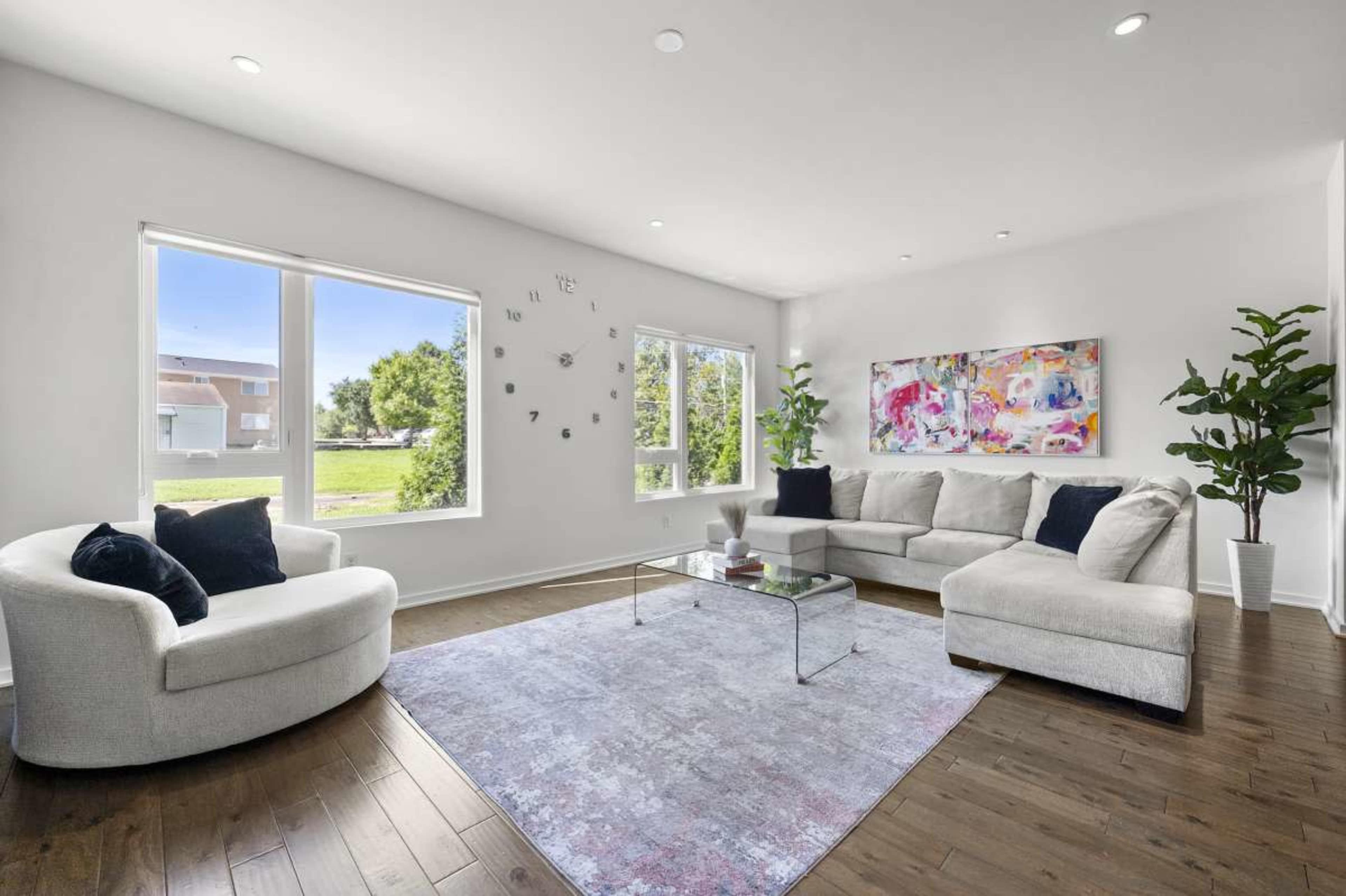 The image shows a modern living room with a light-colored sectional sofa, two armchairs, a glass coffee table, and a large abstract painting on the wall.