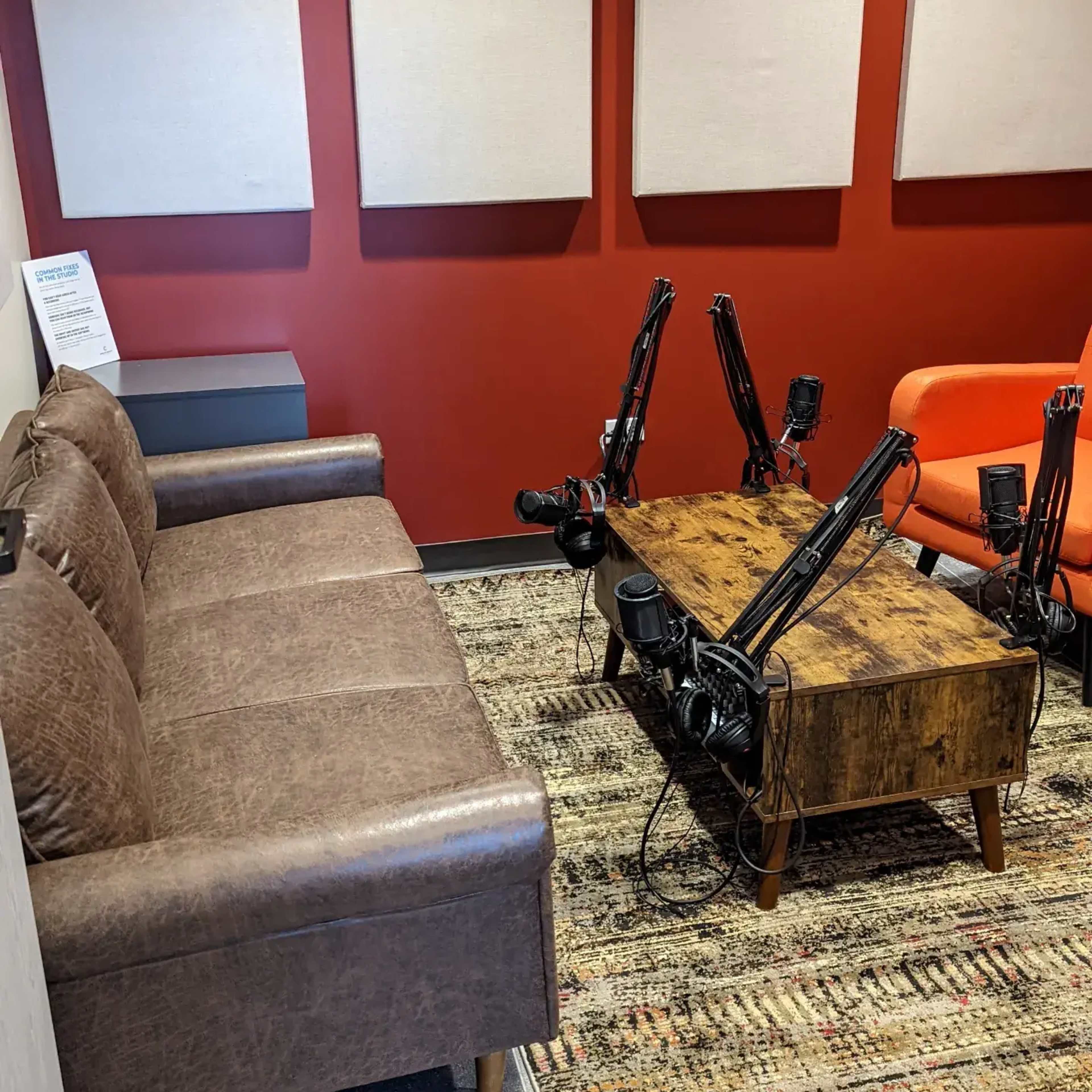 A small room with a brown leather couch, an orange armchair, a wooden coffee table, and multiple camera tripods set up around the table.