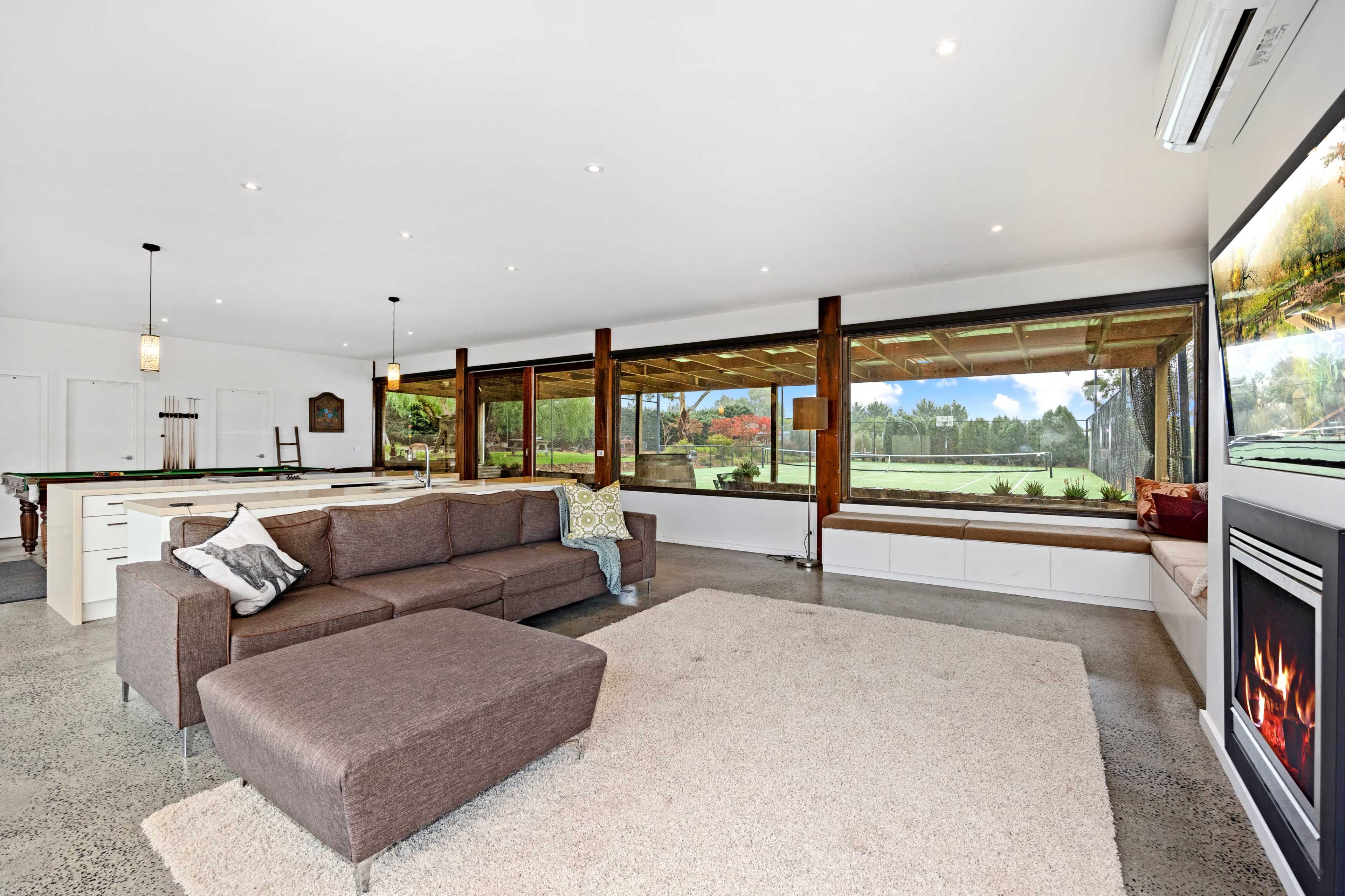 The spacious living area features a sectional sofa, a large rug, and expansive glass windows that provide a view of the outdoor landscape.
