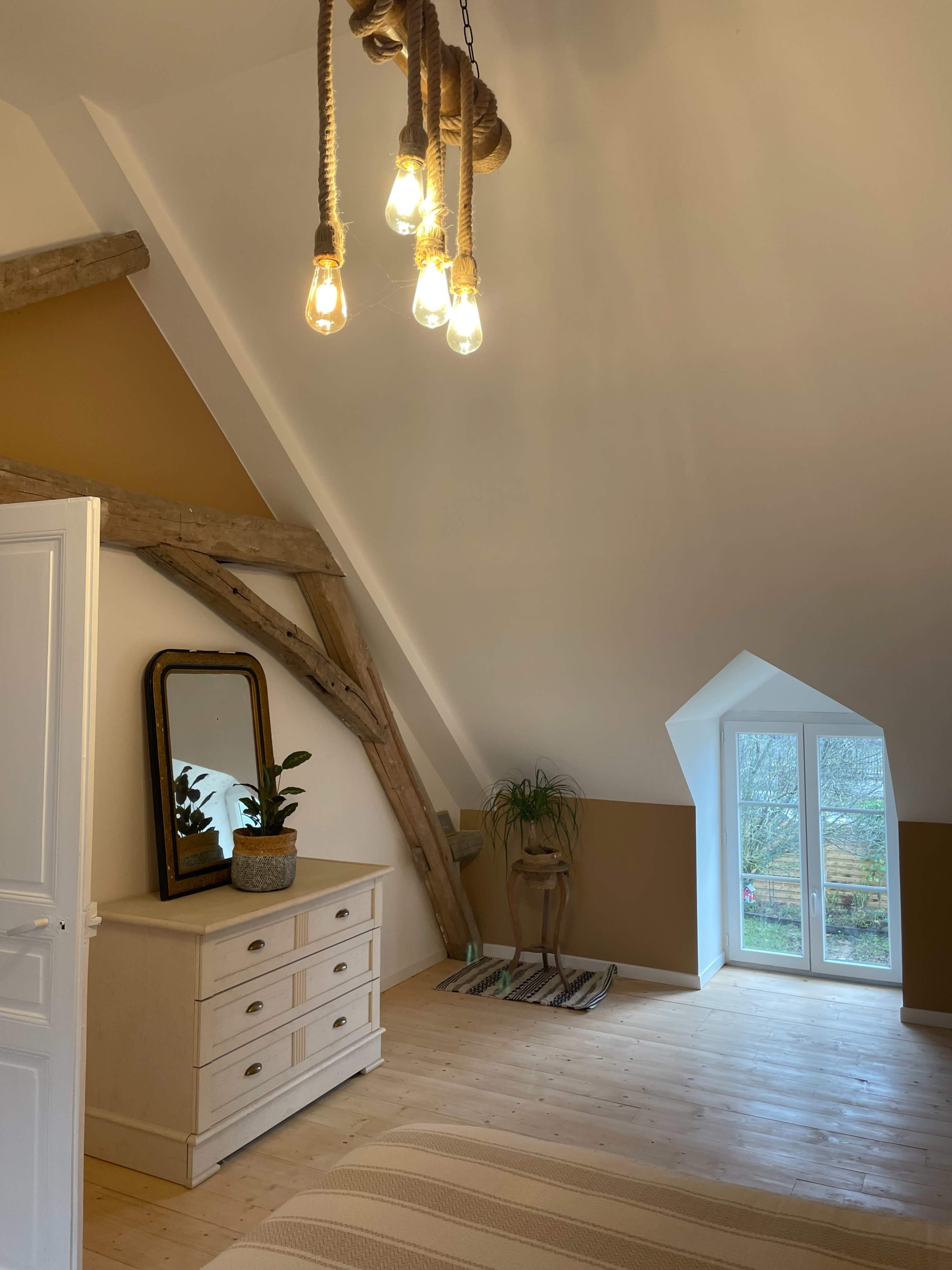 A well-lit attic bedroom featuring a dresser, a mirror, and large windows with a view.