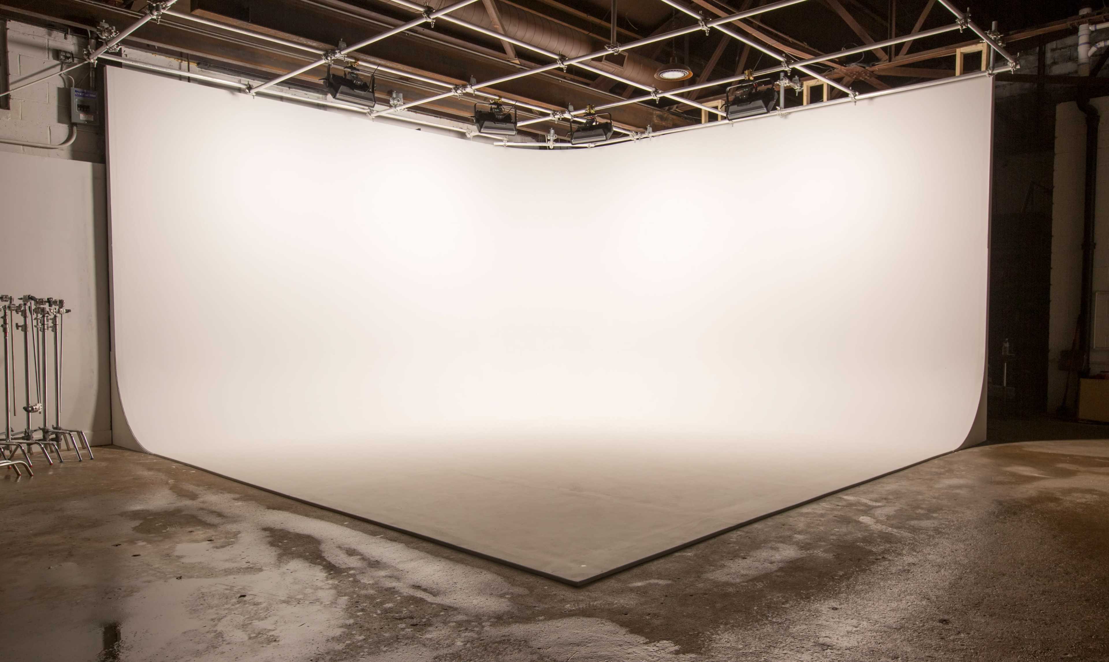 A large, empty studio space with a seamless white backdrop and concrete flooring.