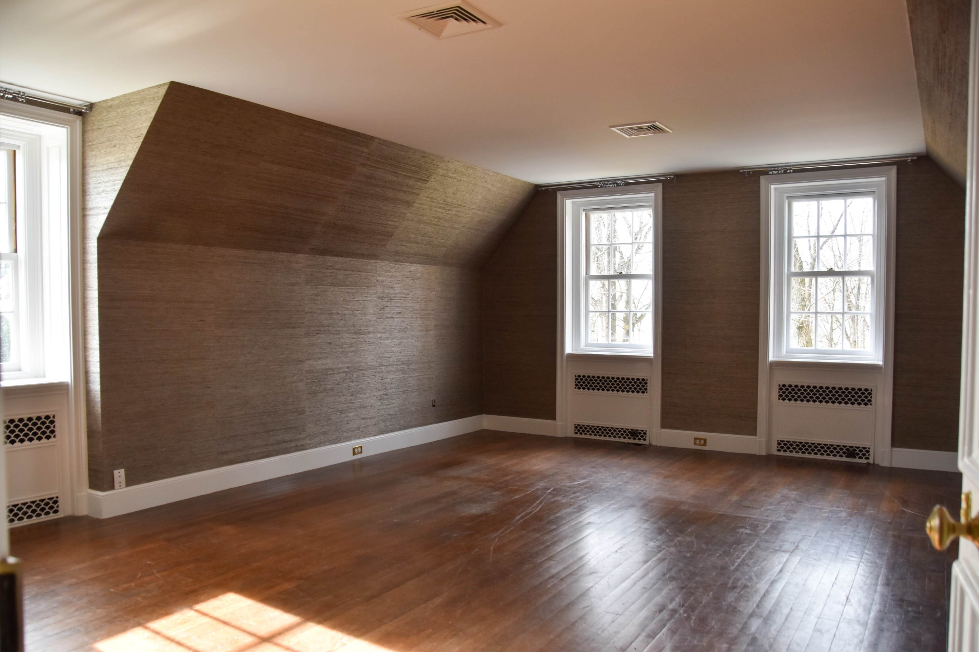 An empty room with sloped walls, two windows, and wooden flooring.