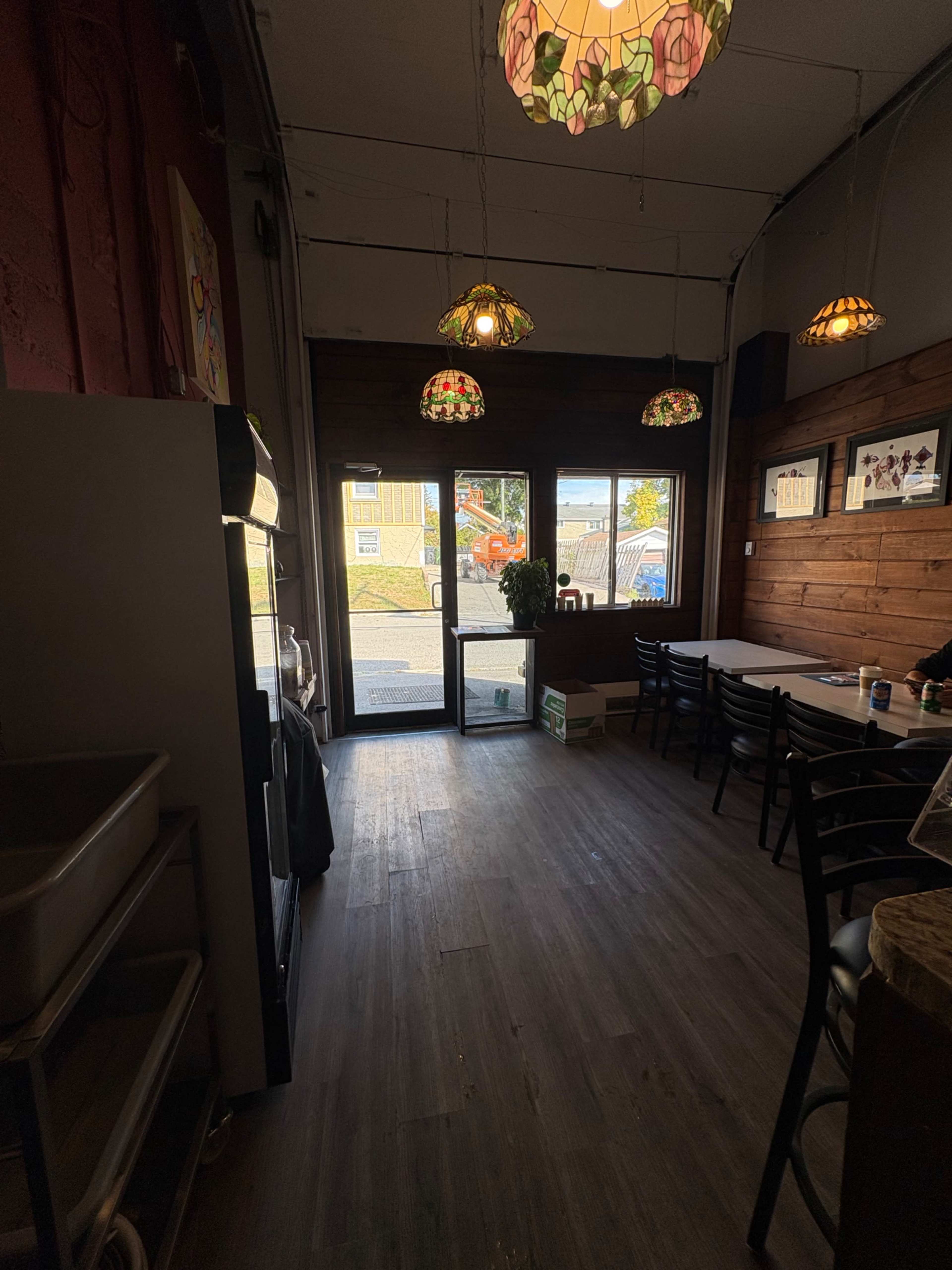 The image shows the interior of a cafe with wooden walls, a row of chairs and tables, and decorative stained glass light fixtures hanging from the ceiling.