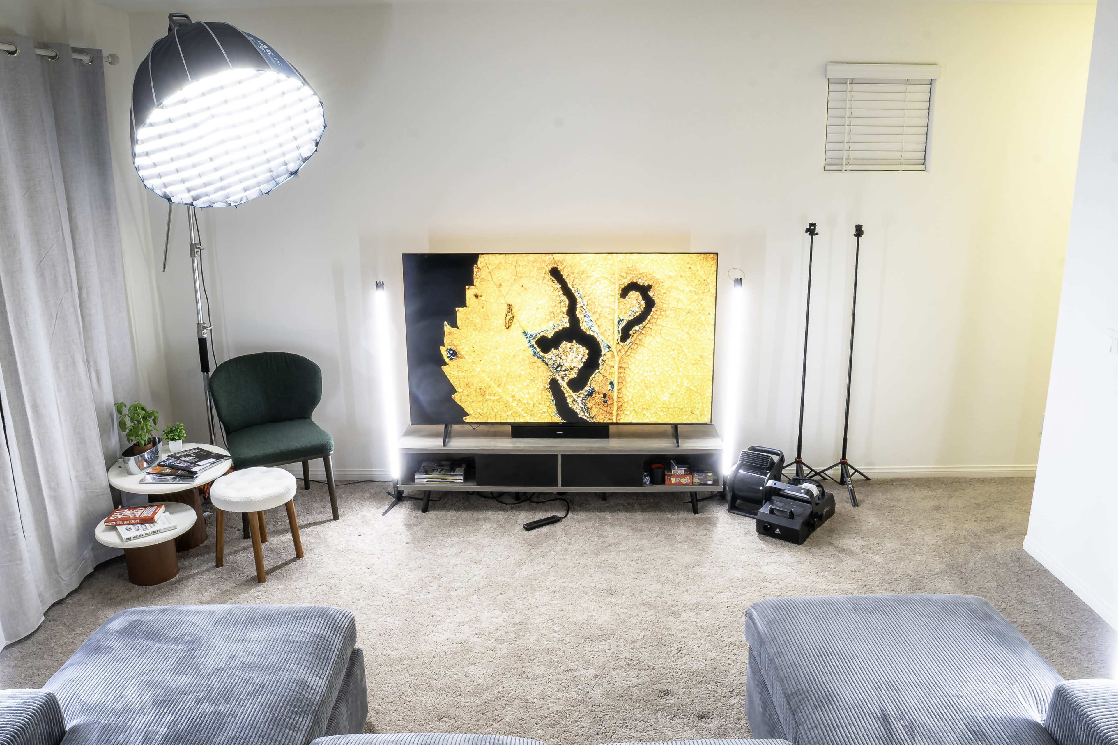 A modern living room features a large television displaying a vibrant image, with a green chair, small tables, and a lamp in the foreground, against a carpeted floor.
