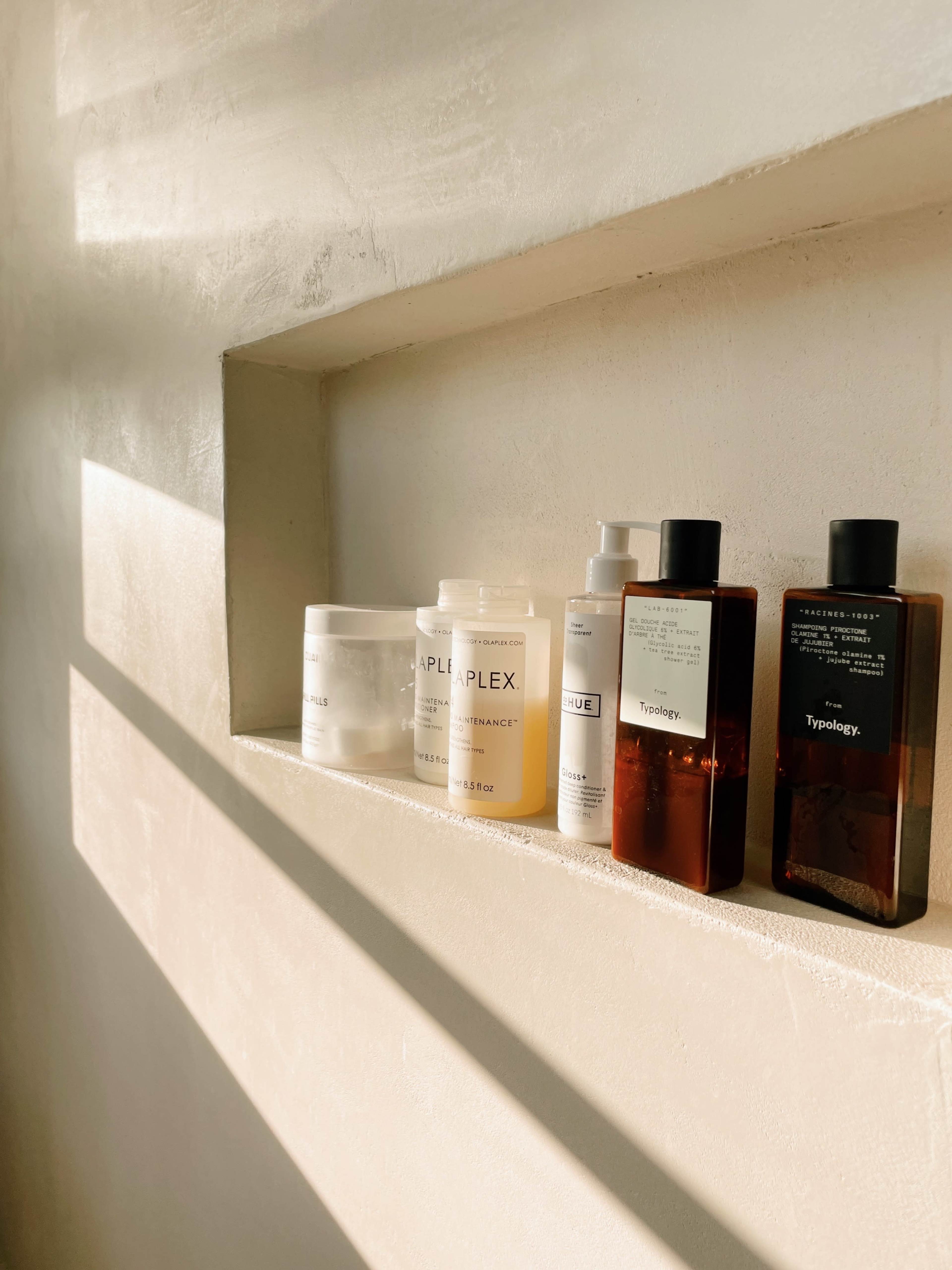 A row of skincare and haircare products is neatly displayed on a shelf with soft sunlight casting shadows.