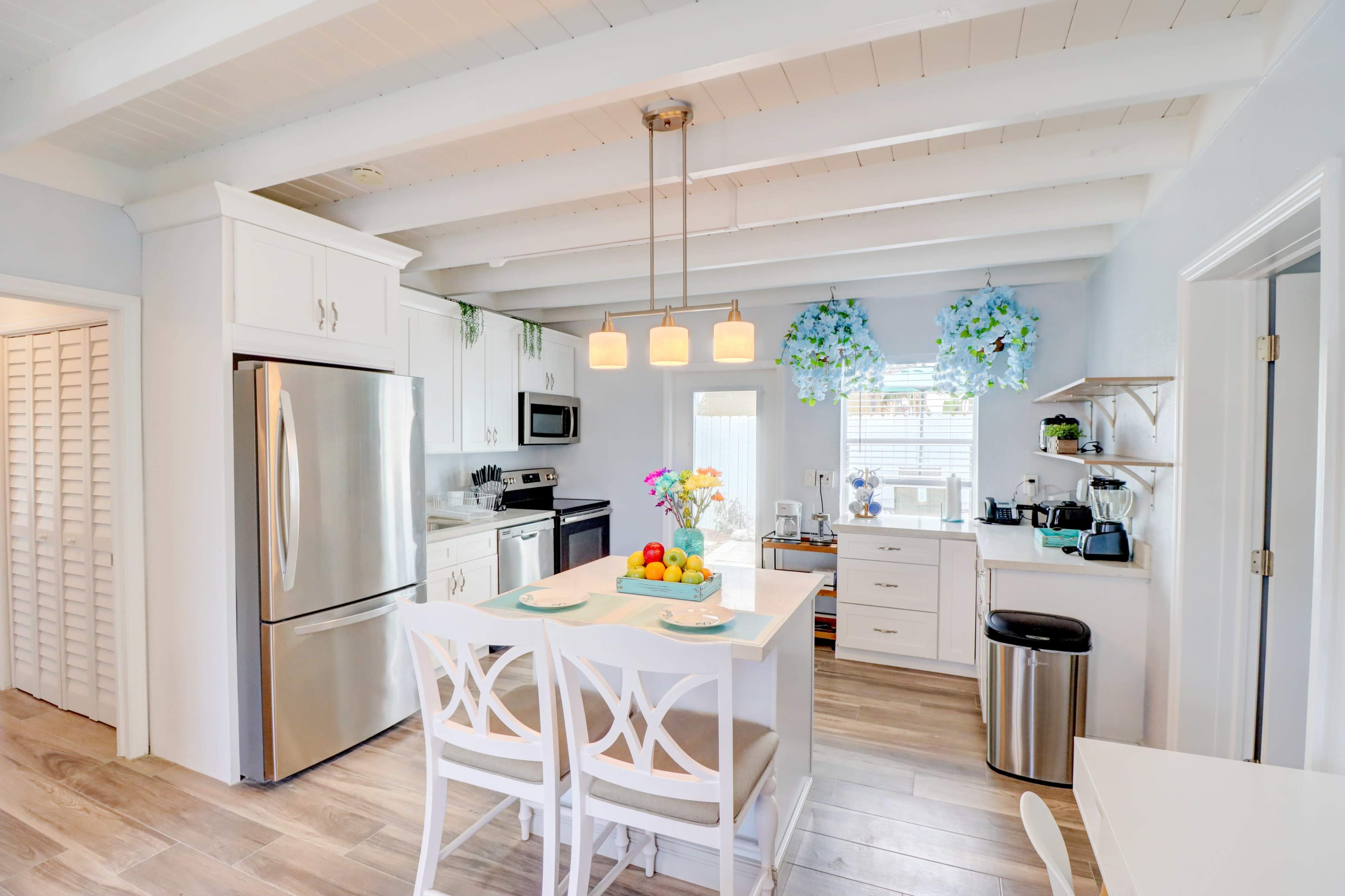 The kitchen features white cabinetry, stainless steel appliances, and a central island with seating, illuminated by pendant lights.