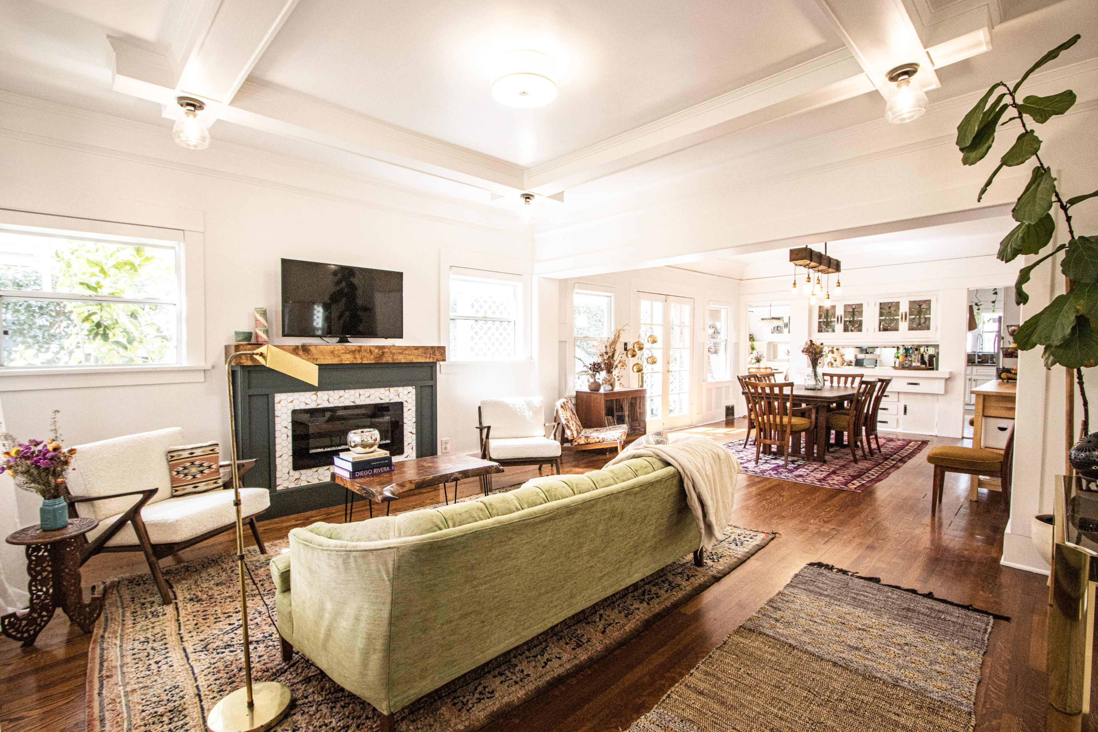 A bright living room with a green sofa, a fireplace, and a dining area visible in the background.