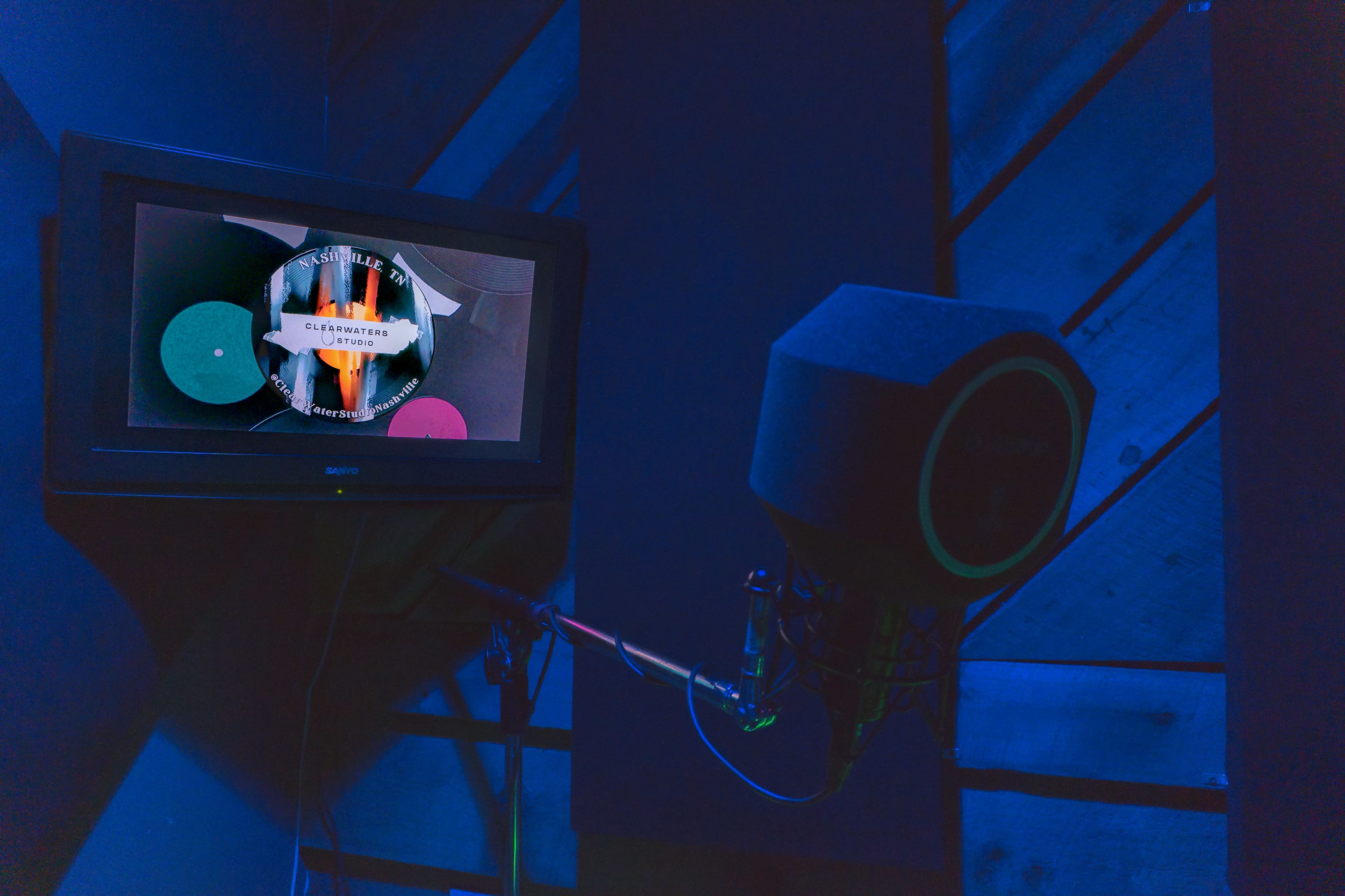 A microphone is positioned near a television displaying a colorful graphic in a sound booth.