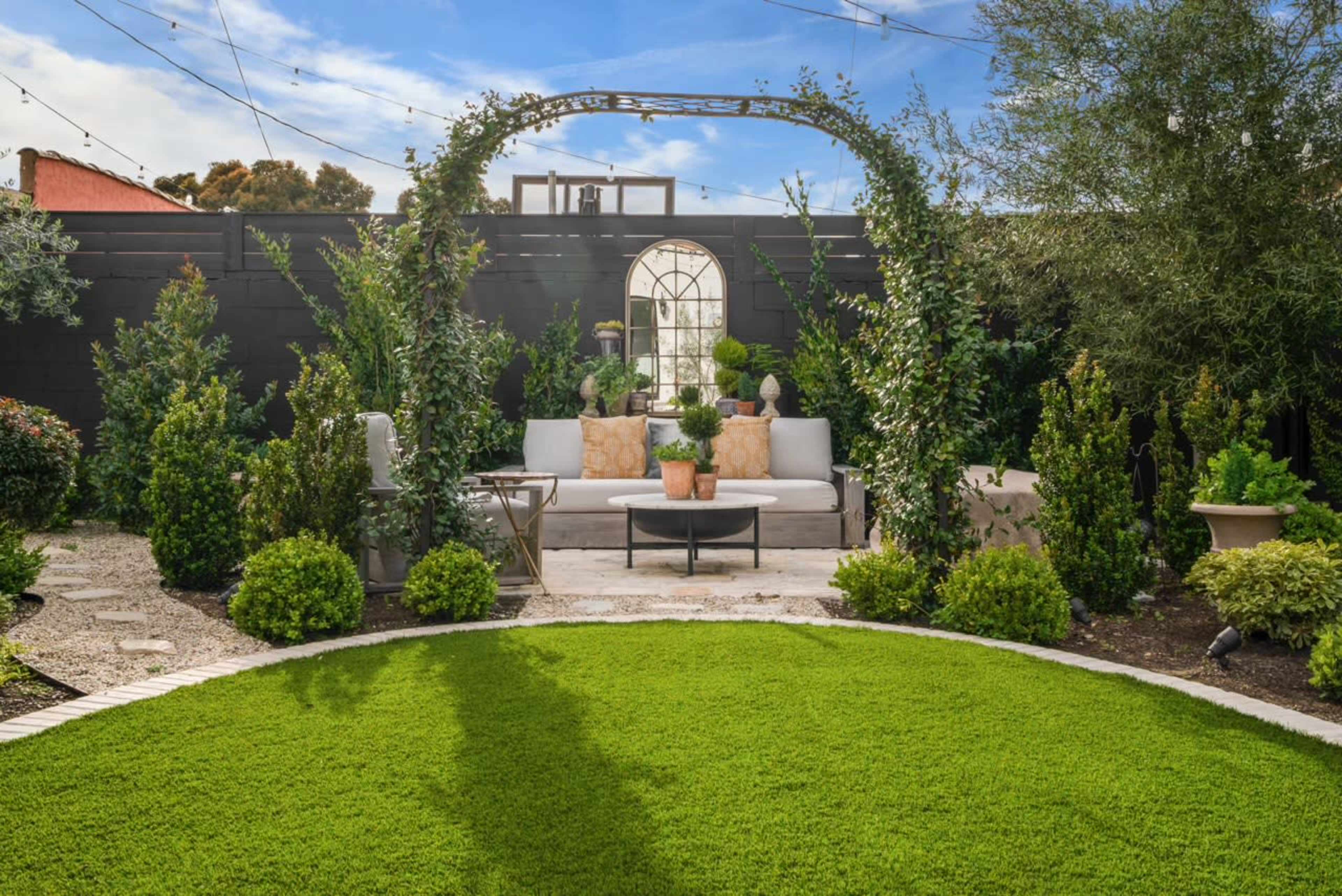 A landscaped garden featuring a curved stone seating area surrounded by greenery and an archway adorned with plants.