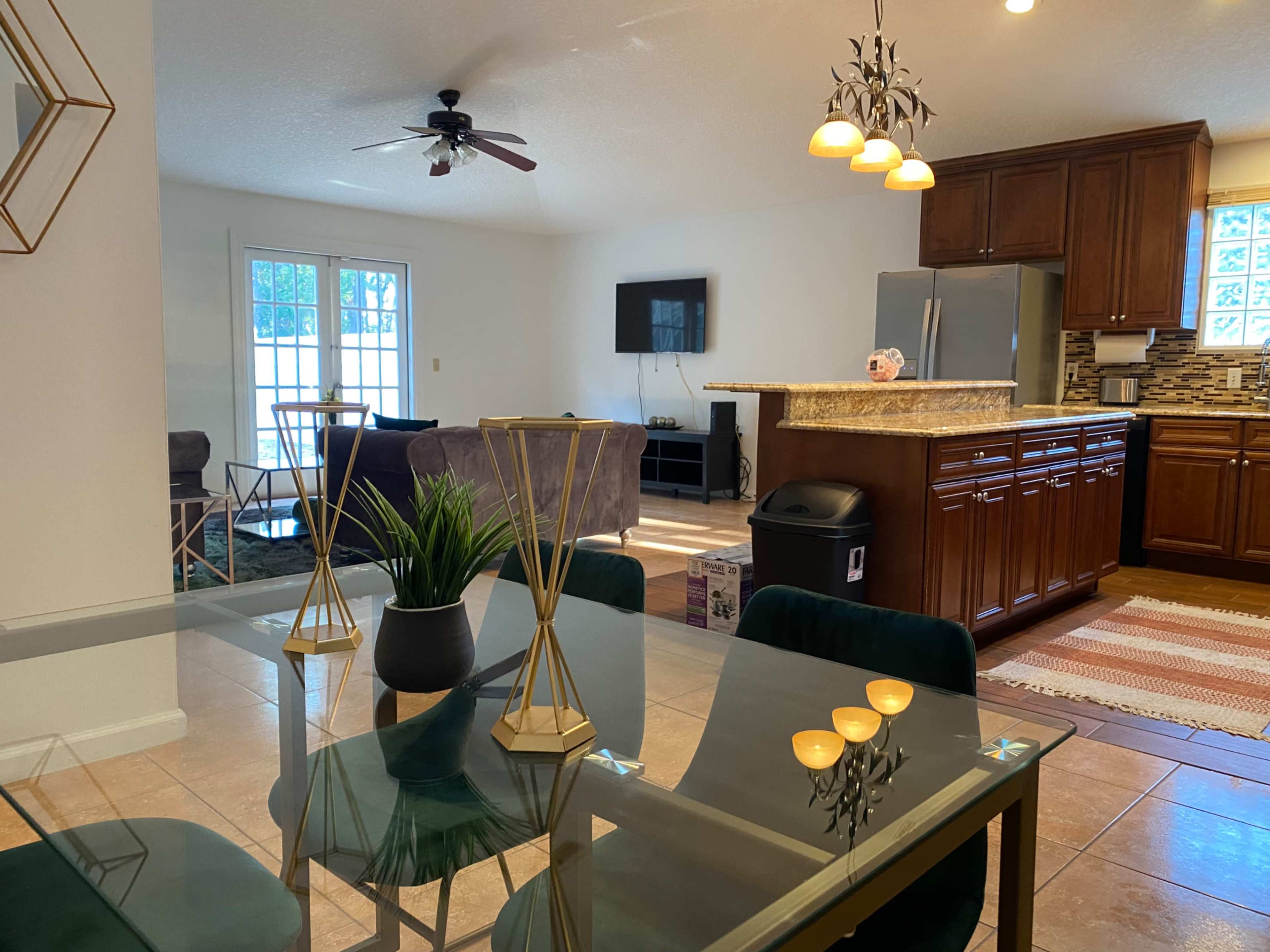 A spacious living and dining area features a glass dining table, a kitchen with wooden cabinets, and a seating area with plush couches.