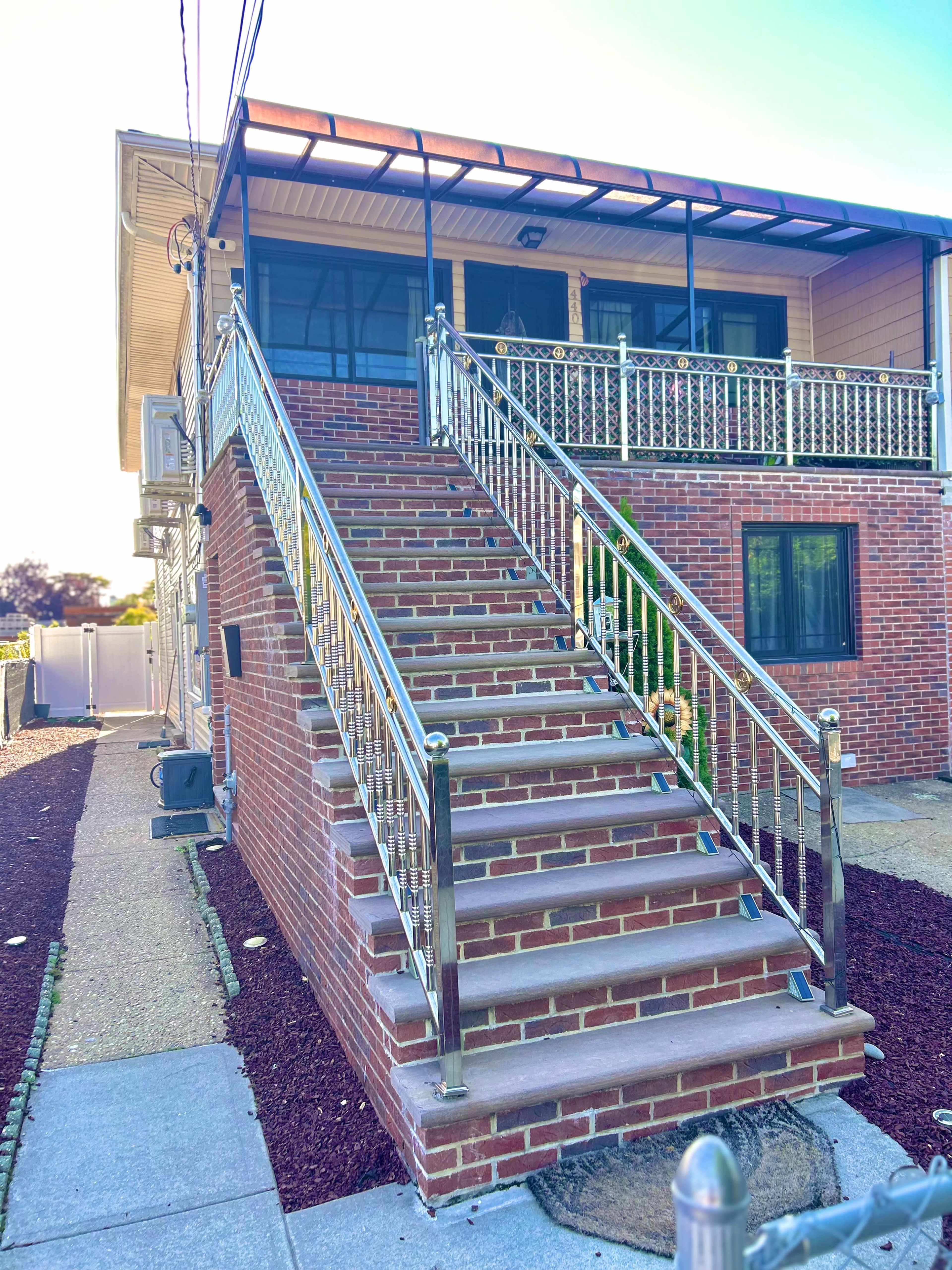 The image shows a two-story brick house with a set of metal-railed stairs leading to a covered porch.