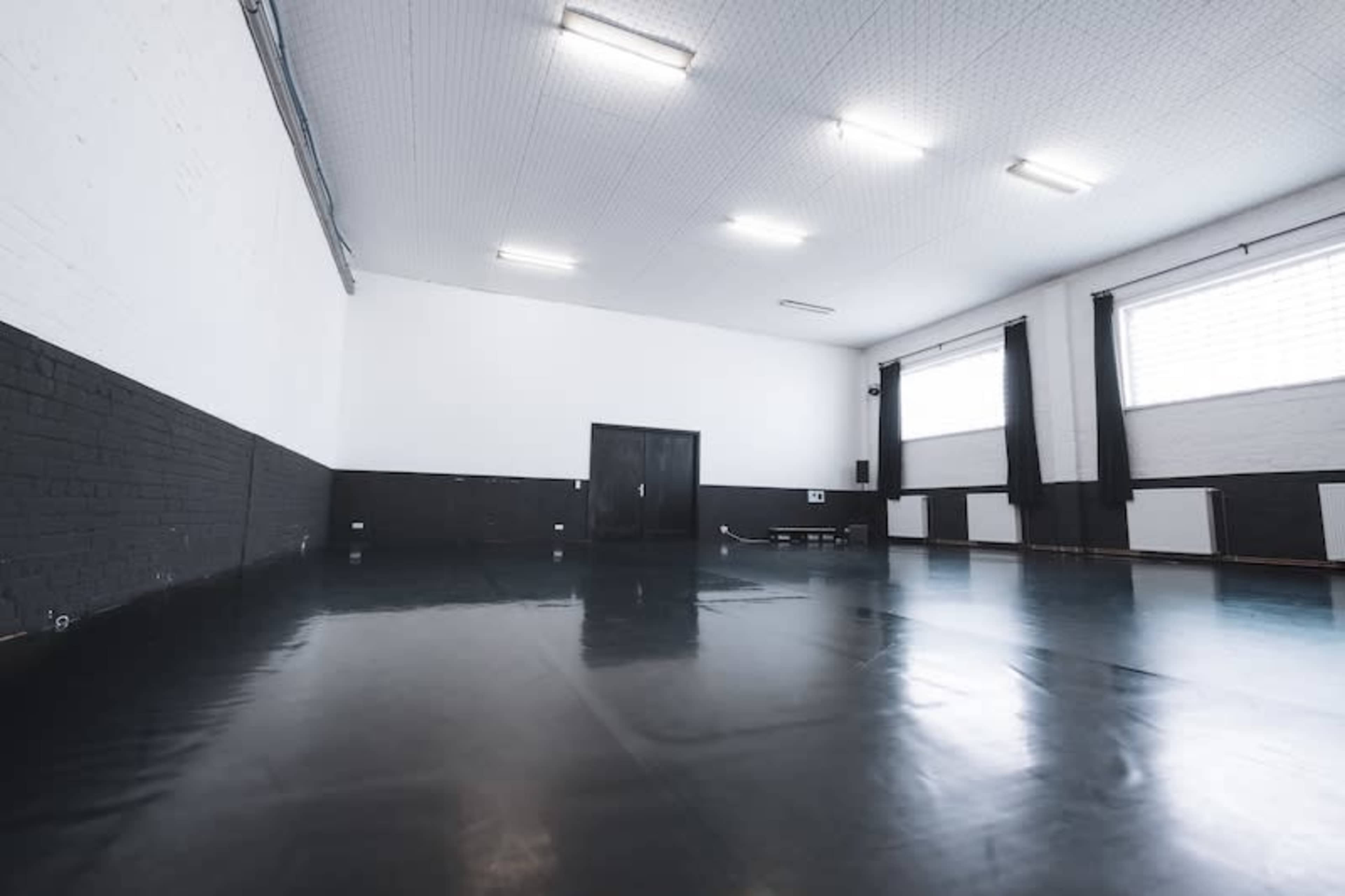 A spacious, empty studio with black and white walls, large windows, and a polished floor.
