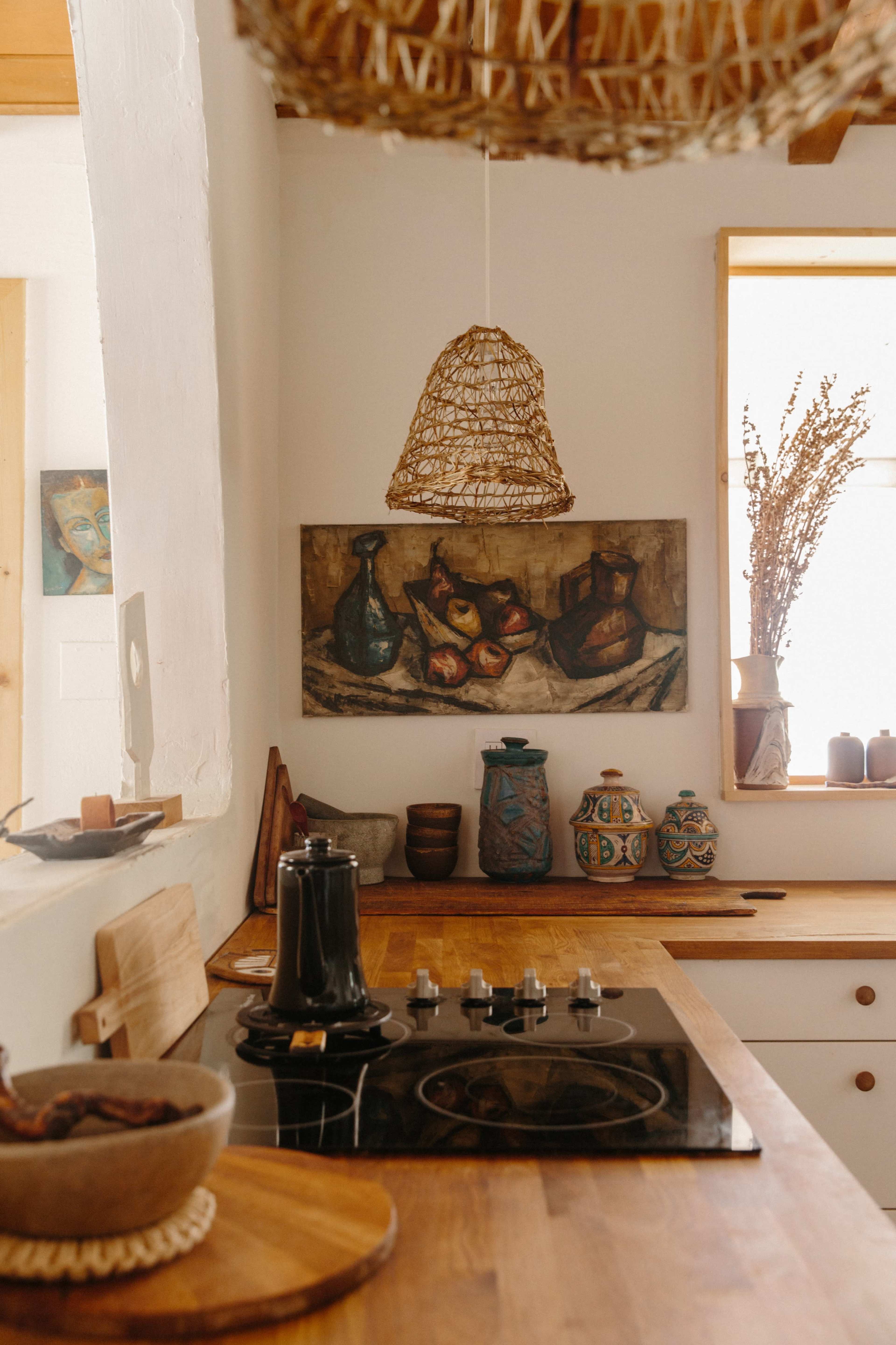 A cozy kitchen with a wooden countertop, a stovetop, and various decorative items, including pottery and artwork on the walls.