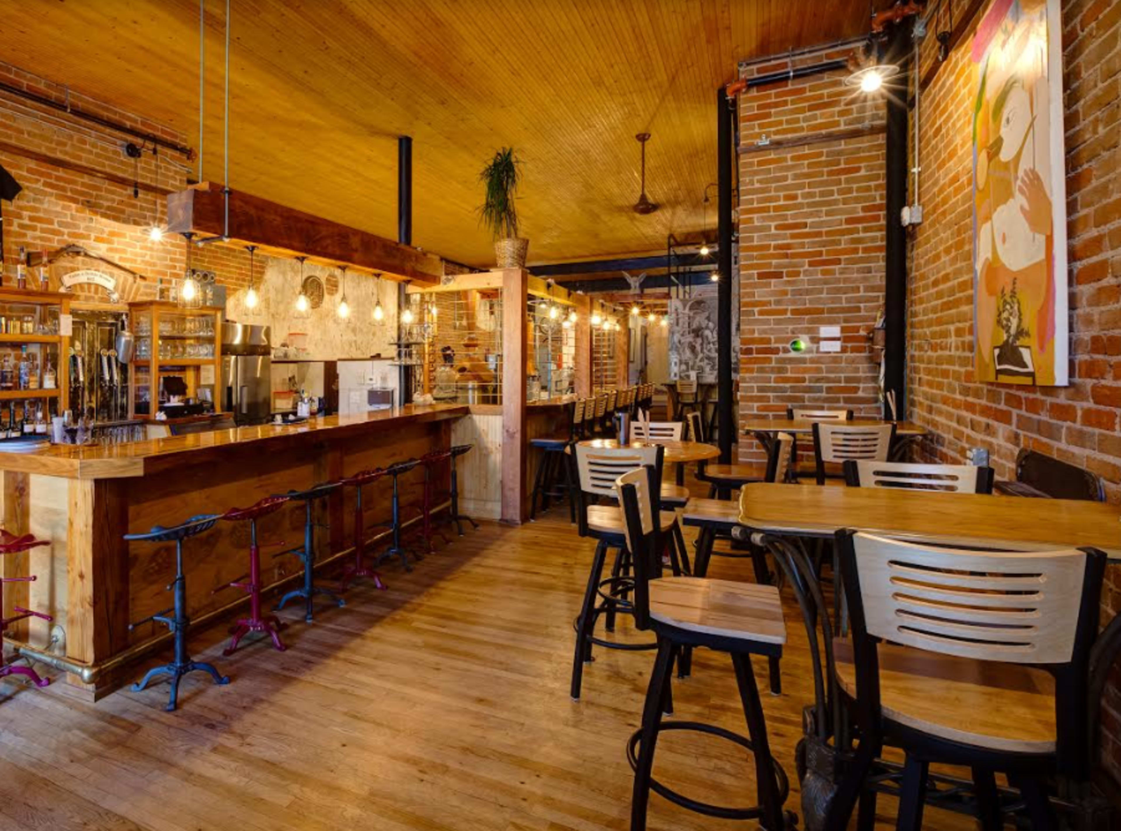 A rustic cafe interior with wooden tables, a bar area, and exposed brick walls.