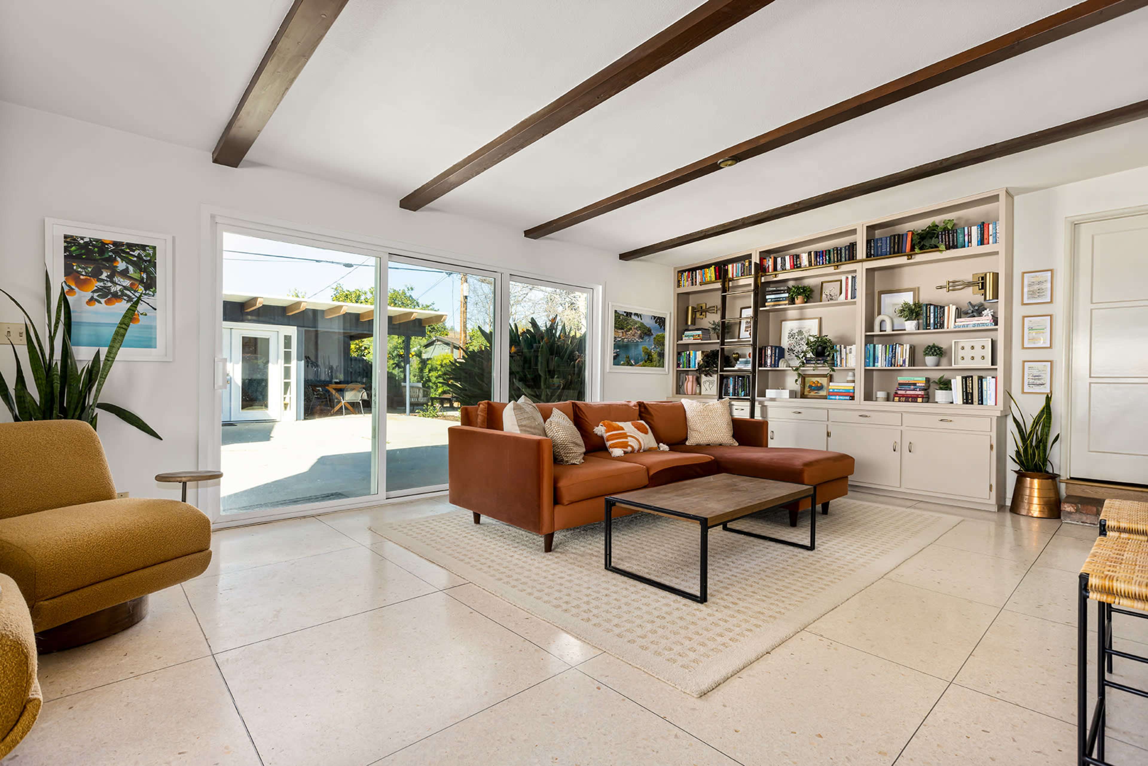A modern living room with a brown sectional sofa, a coffee table, built-in shelves filled with books and decor, and large windows overlooking an outdoor patio.