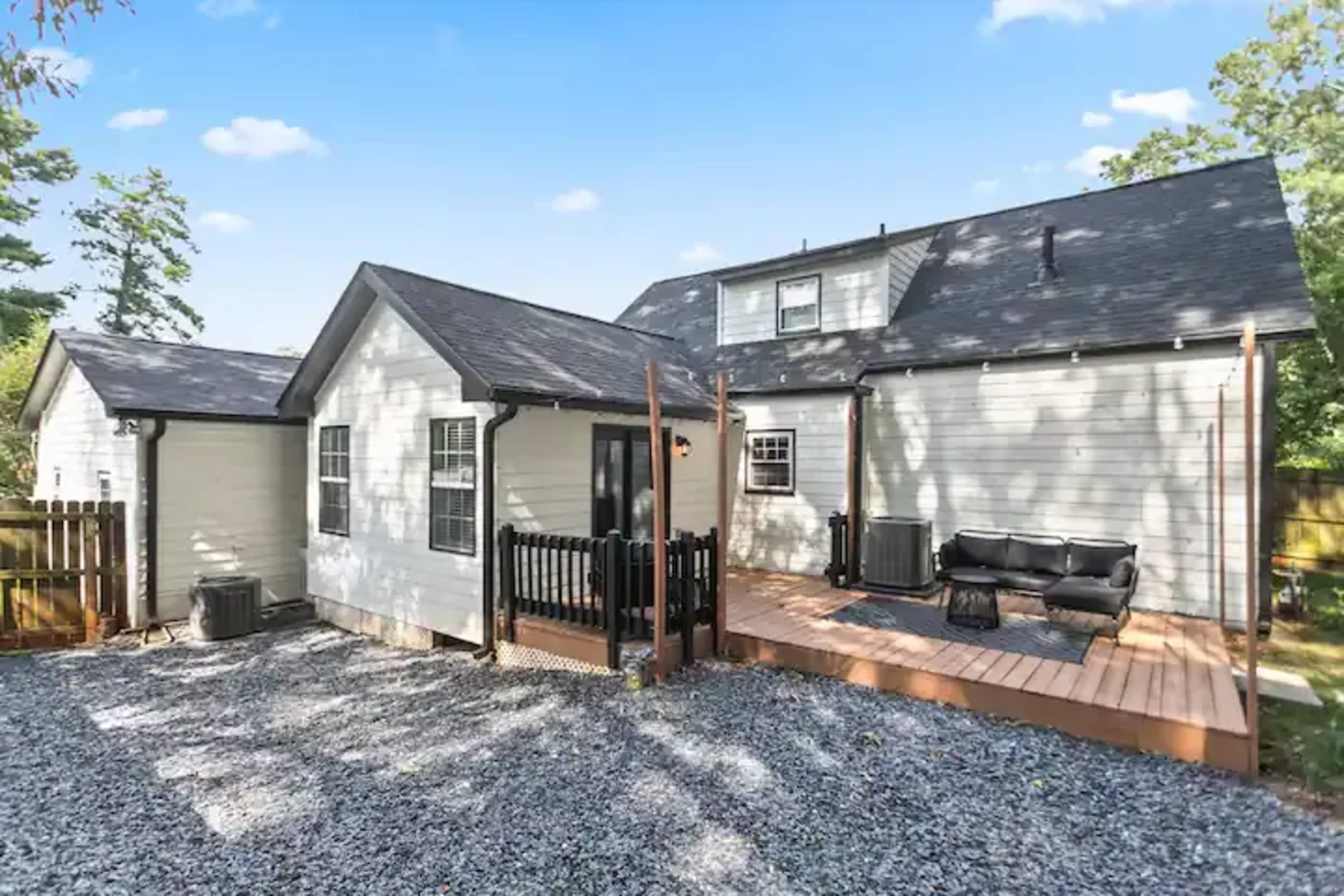 A gray gravel yard features a white house with a wooden deck and black seating area in the backyard.