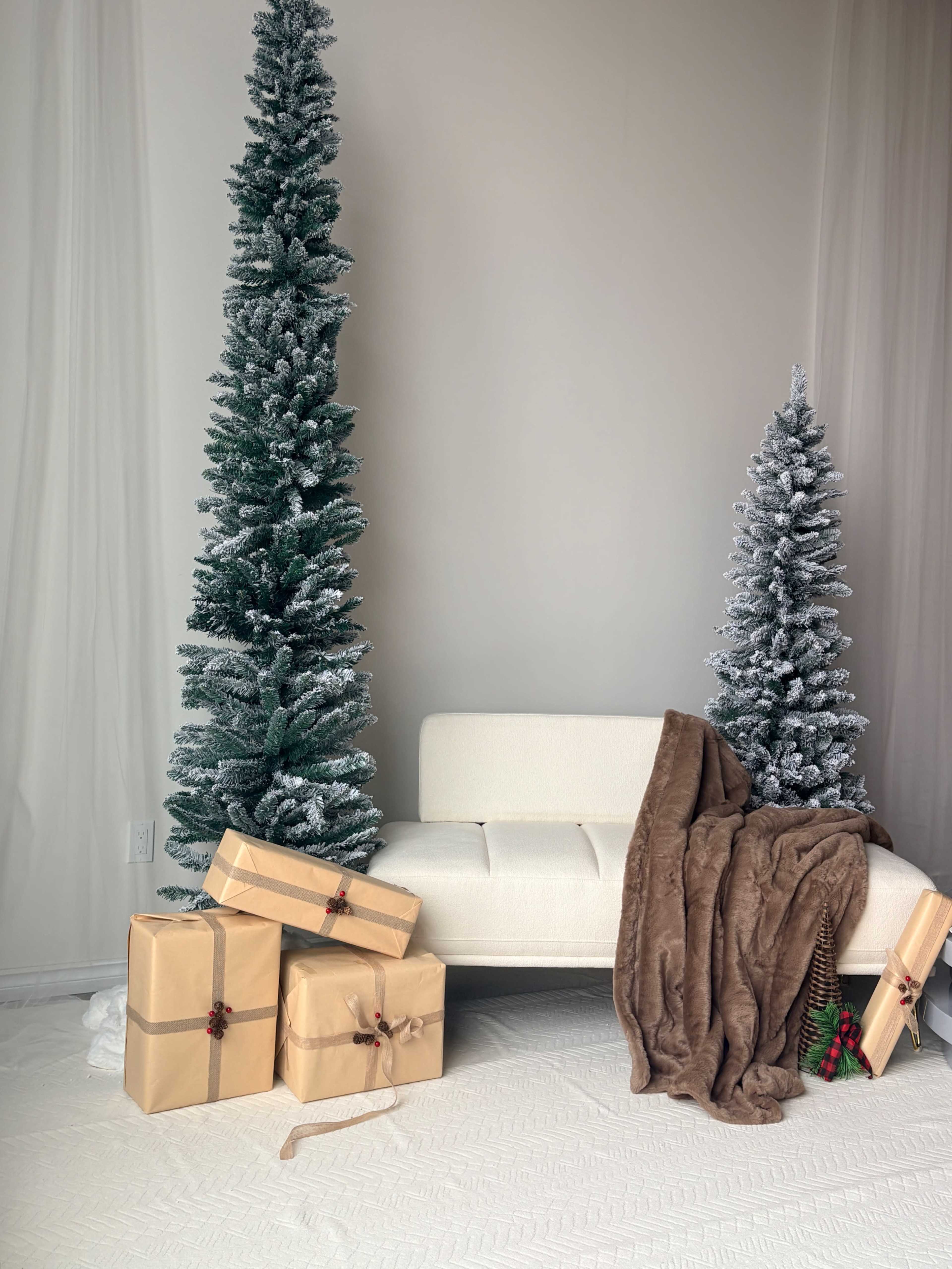 A cozy seating area is decorated with two artificial Christmas trees, wrapped gifts, and a soft brown throw blanket.