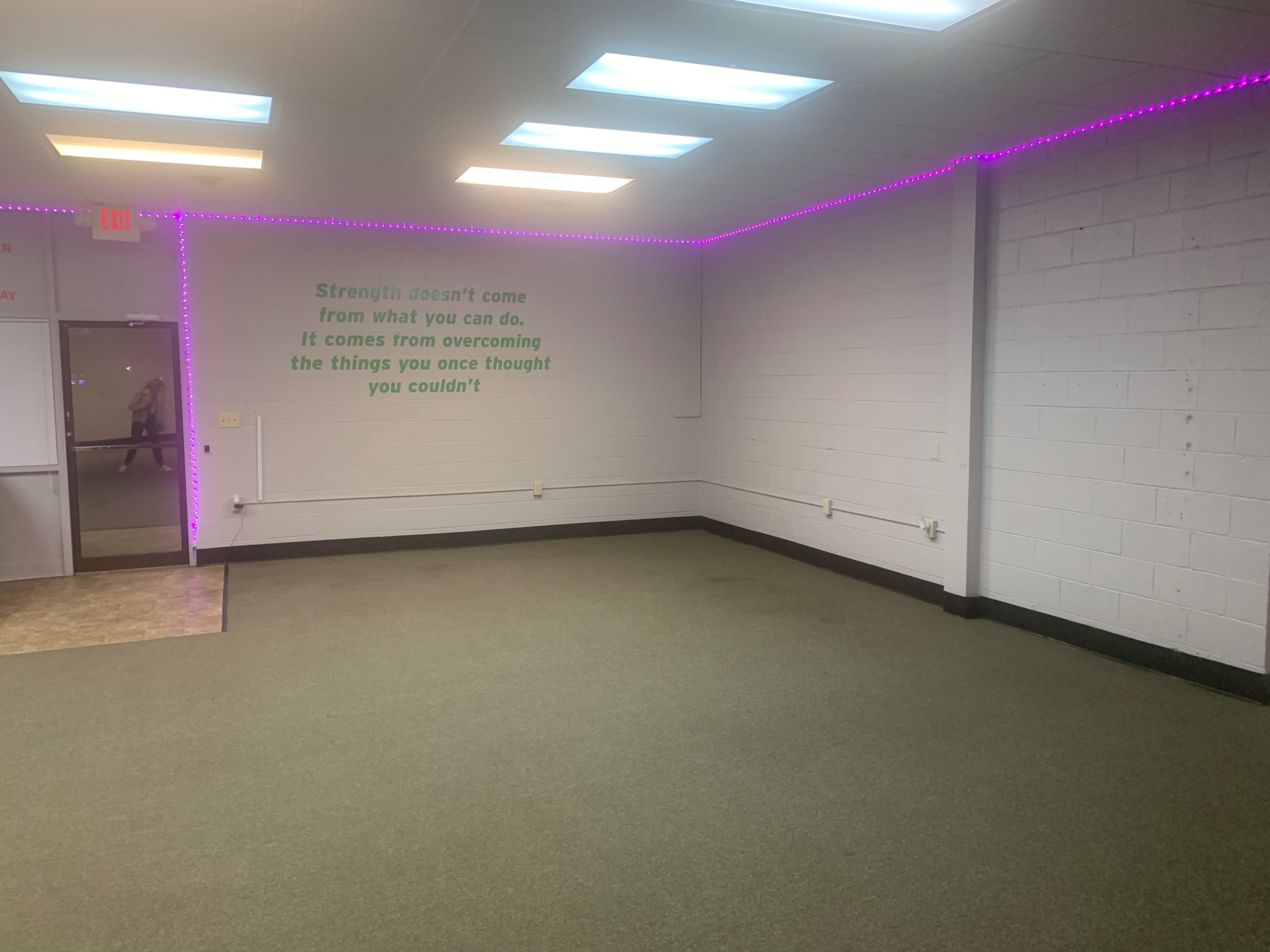 The image shows an empty room with green motivational text on the wall and purple LED lights along the ceiling.