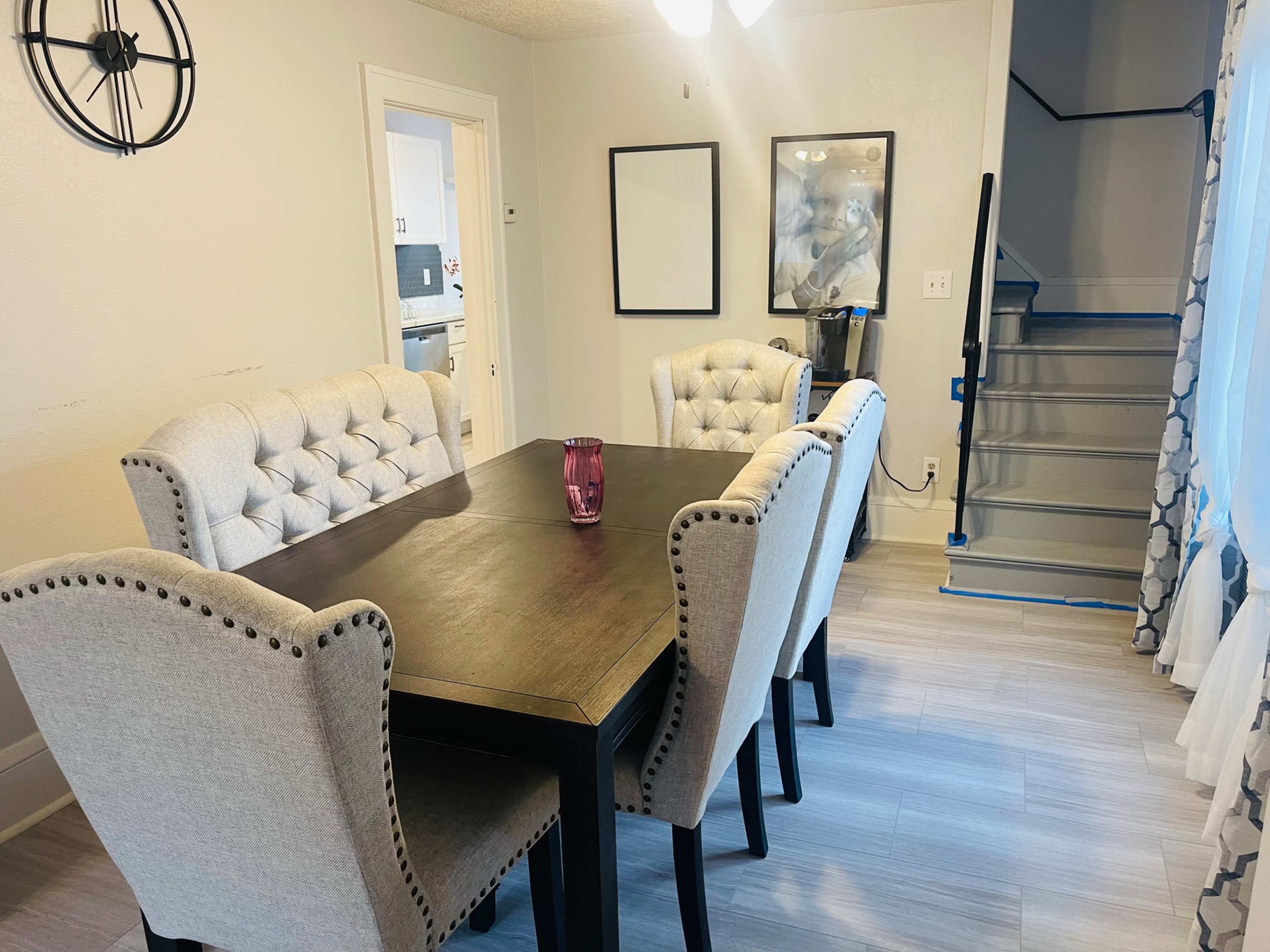 A dining area features a dark wooden table surrounded by five upholstered chairs, with a staircase visible in the background.