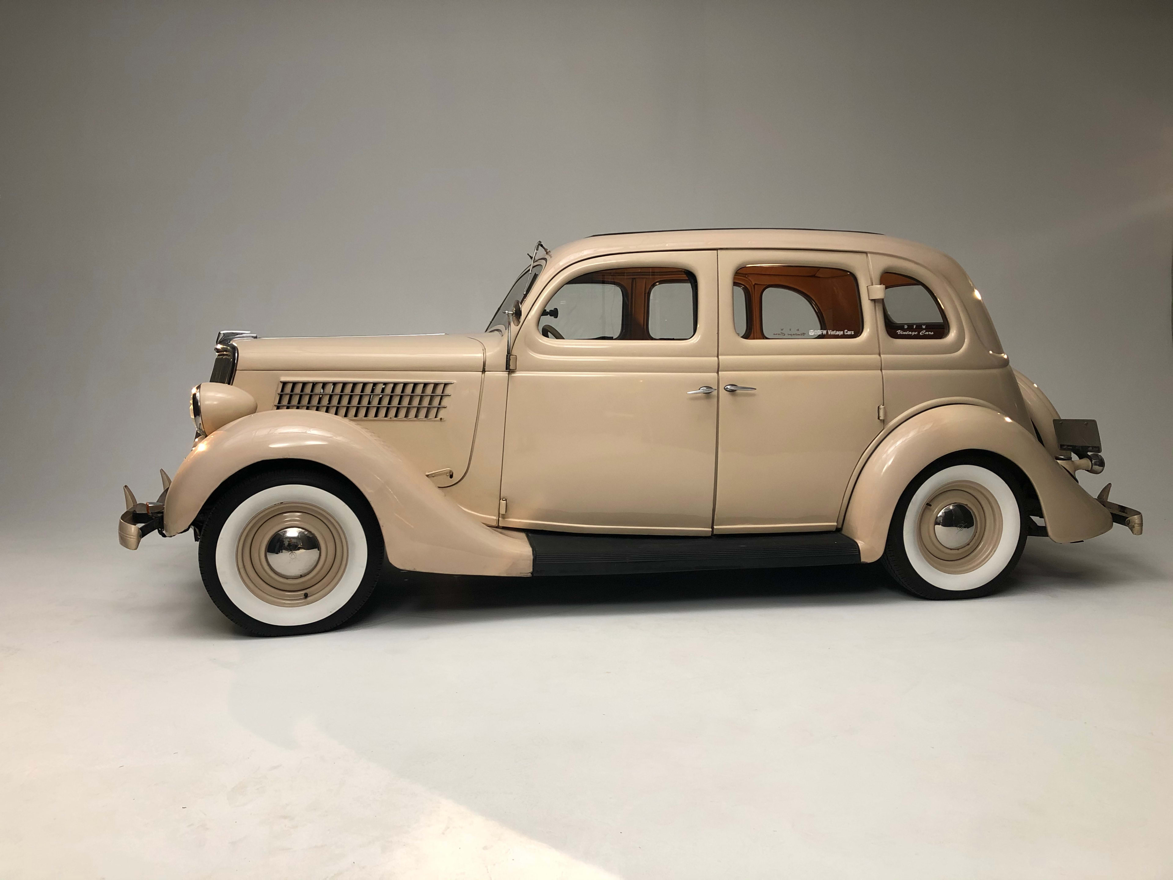 A vintage beige sedan with whitewall tires is positioned against a neutral background.
