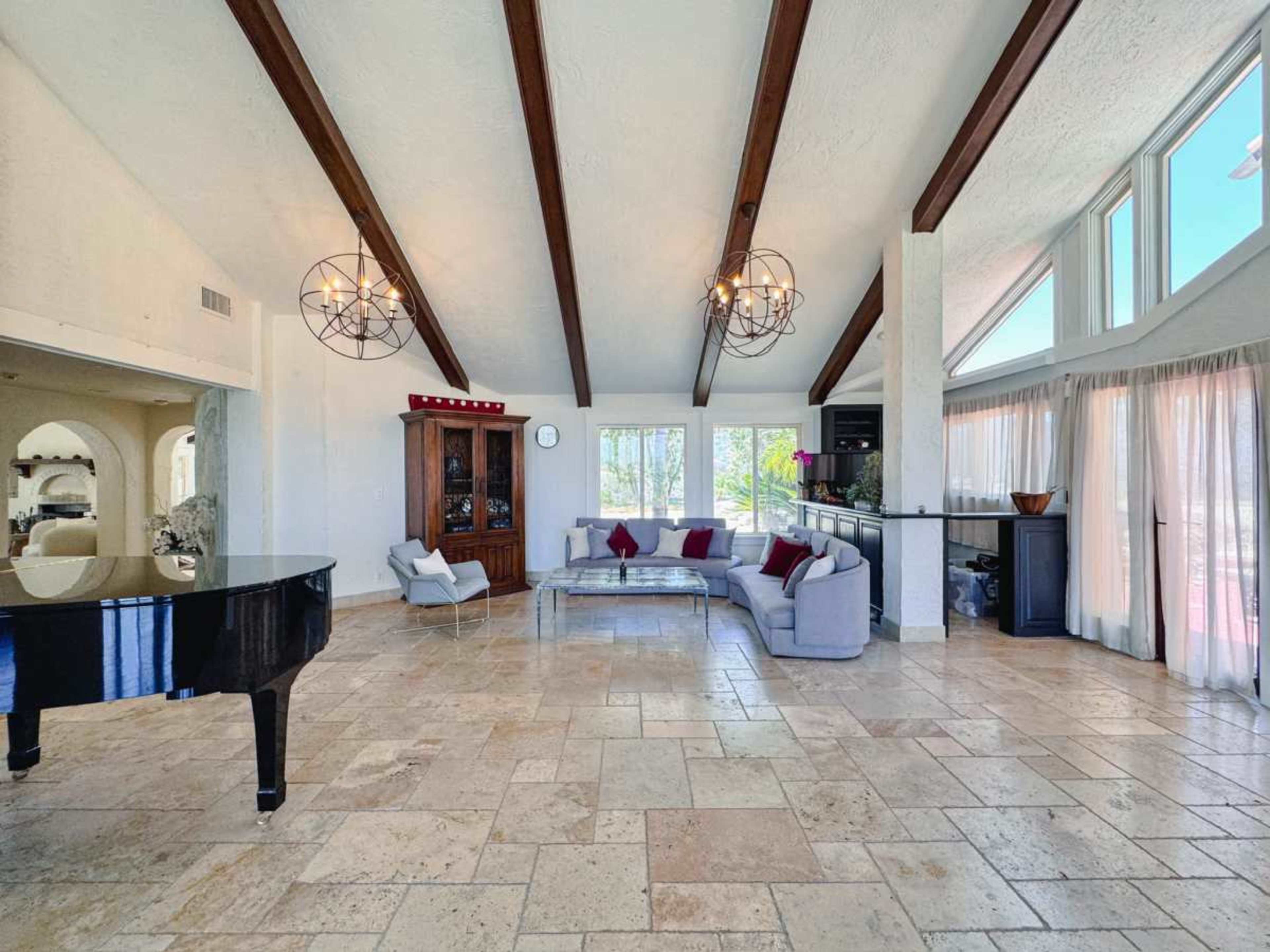 A spacious living room features a grand piano, a sectional sofa, and large windows allowing natural light to fill the space.