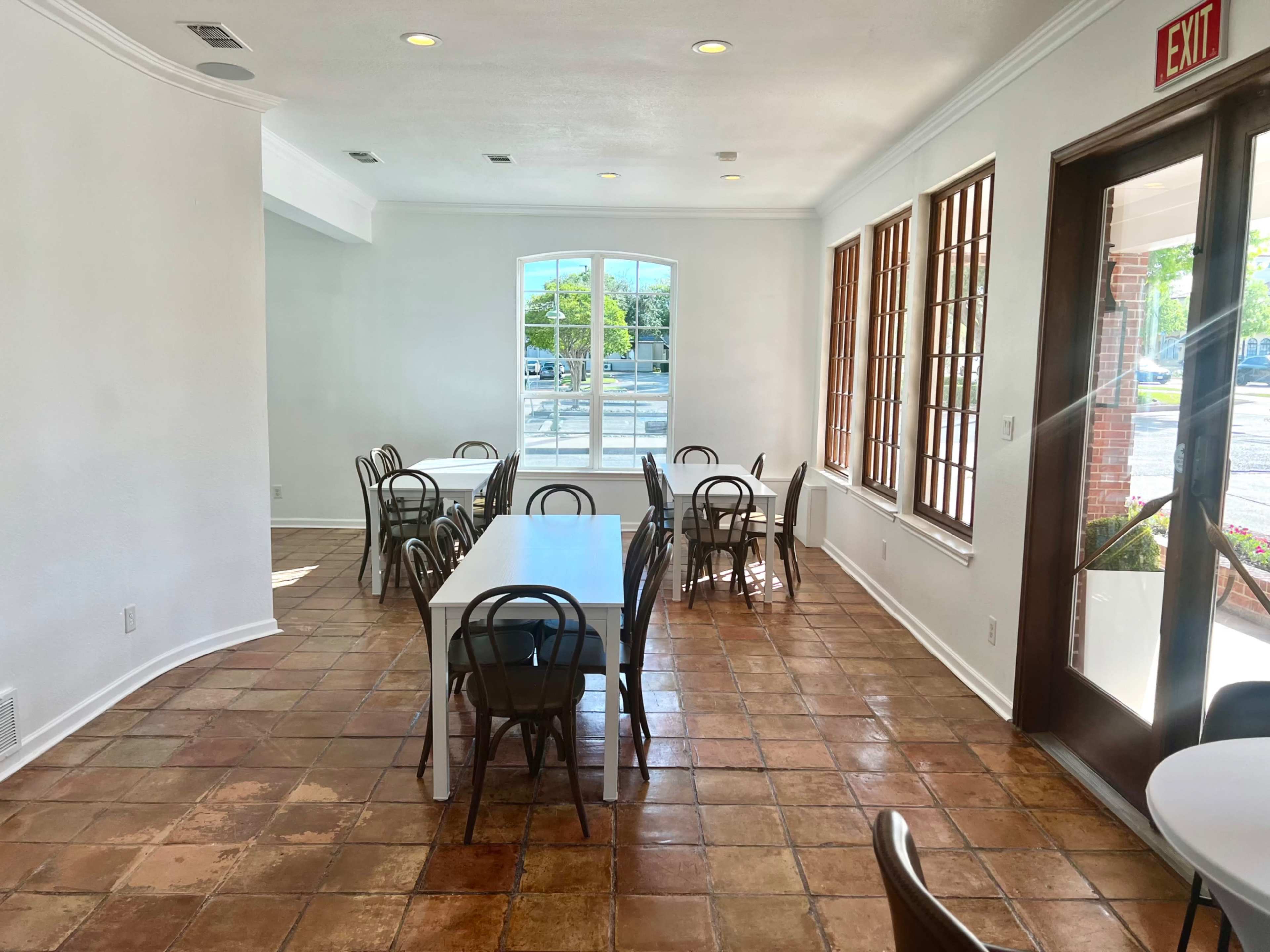 A well-lit dining area with several tables and chairs arranged neatly on tiled flooring.