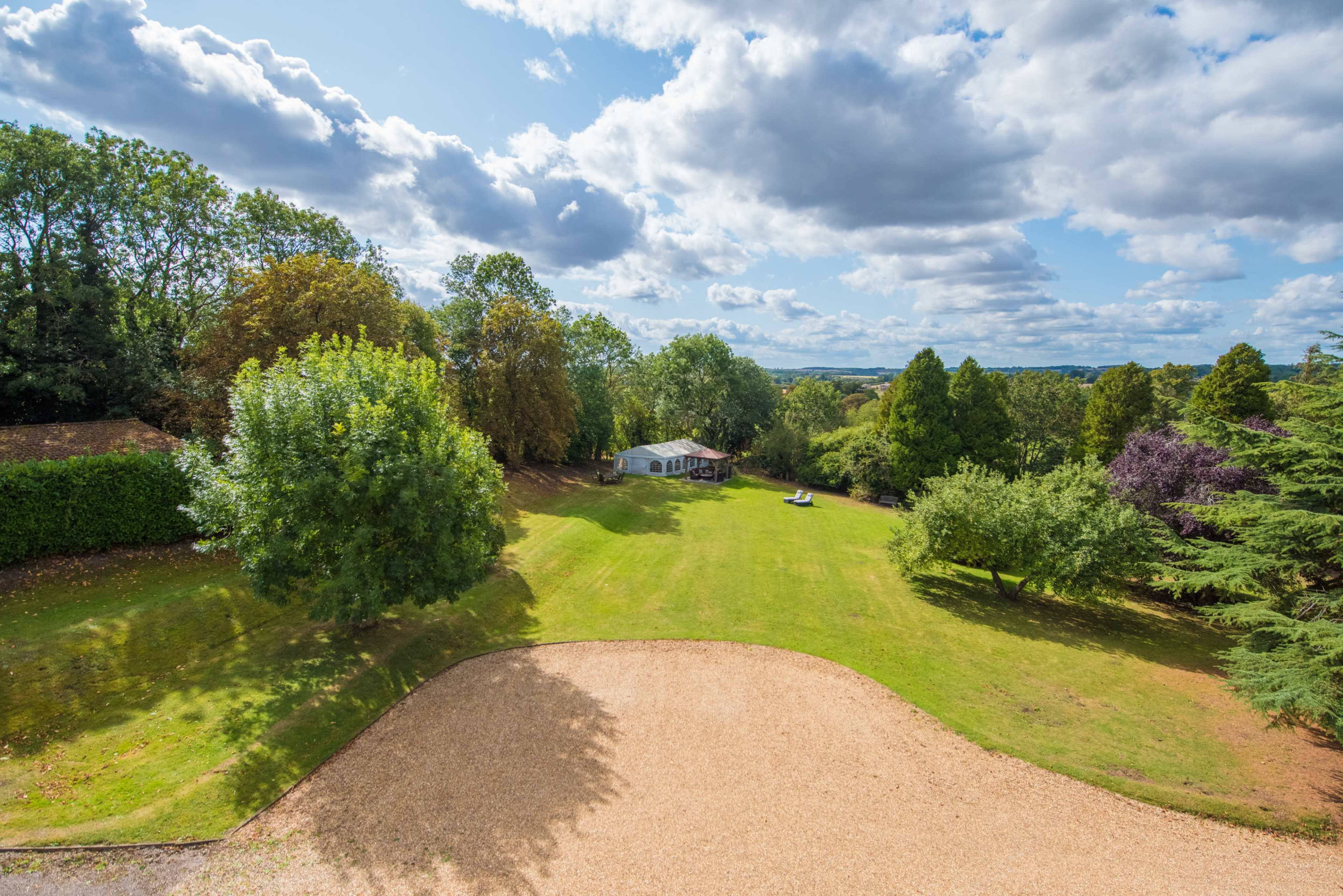 The image shows a grassy landscape with a house in the background, surrounded by trees and under a partly cloudy sky.