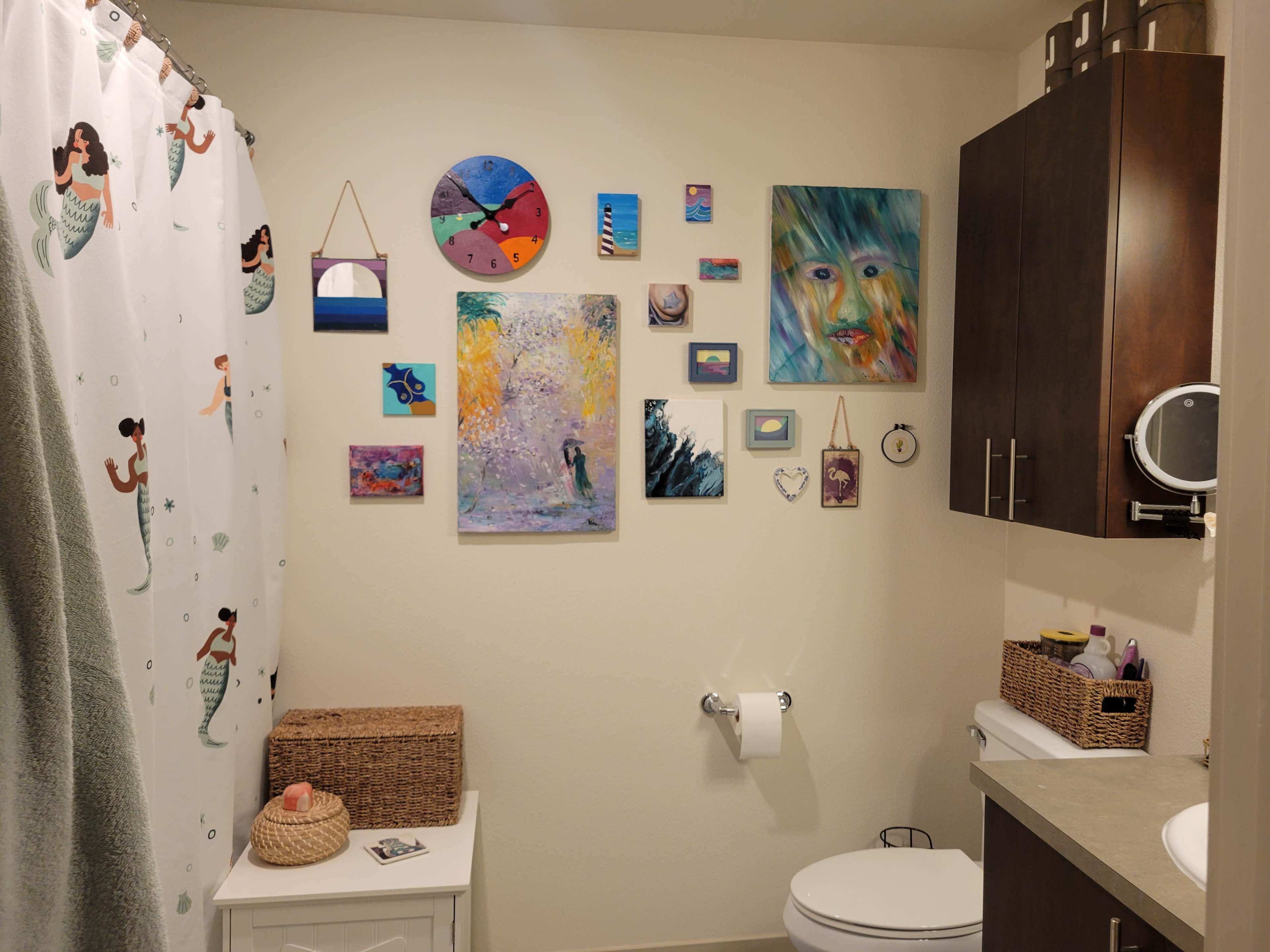 A bathroom featuring a decorated wall with various pieces of artwork and a shower curtain with a mermaid design.