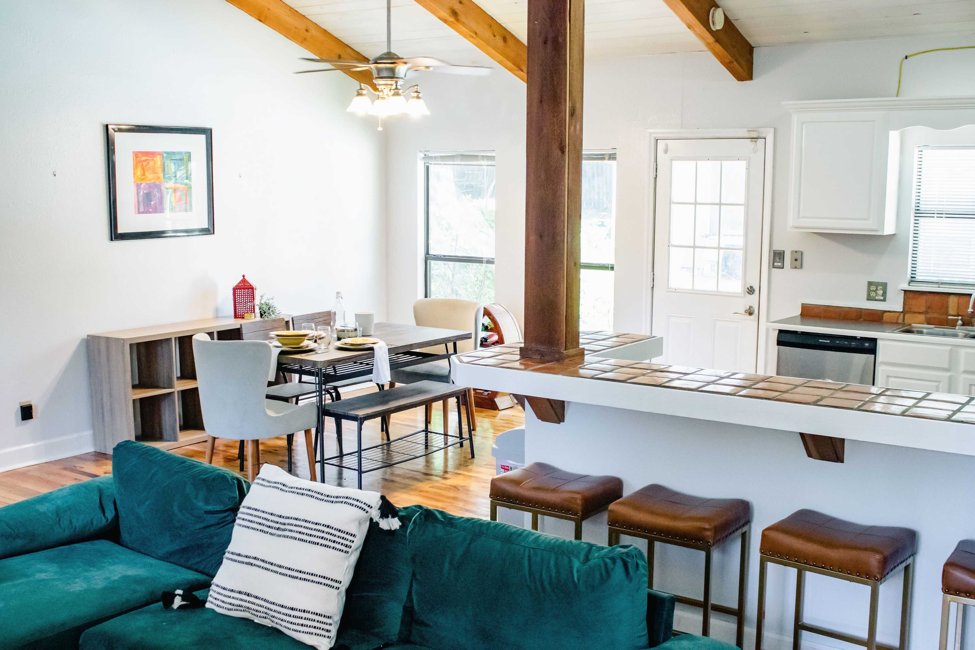 A bright, open-concept living area with a kitchen, dining table, and a seating area featuring a green couch.