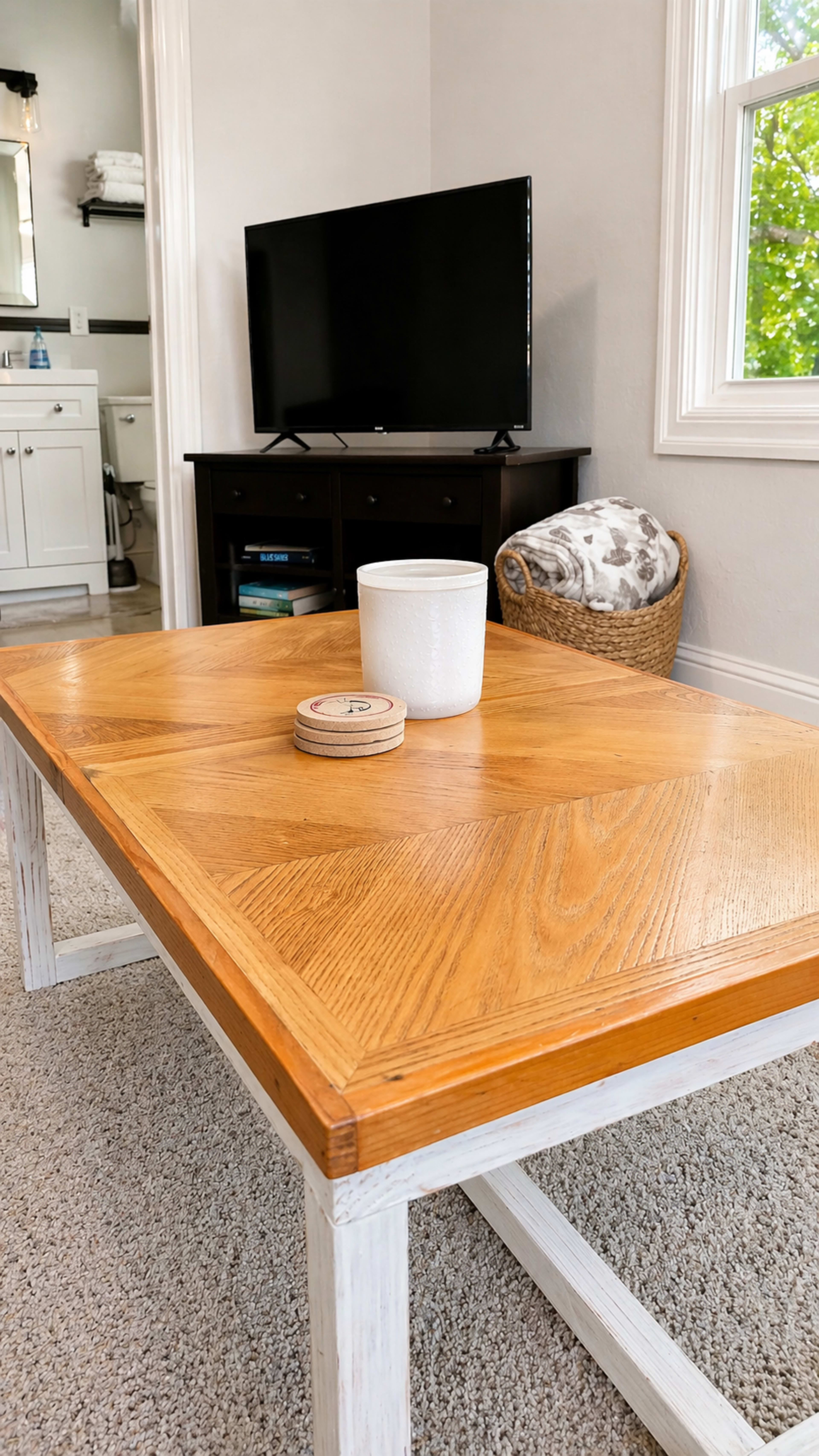 A wooden coffee table with a patterned top is placed in a living room setting, featuring a television on a black stand and a decorative white container on the table.