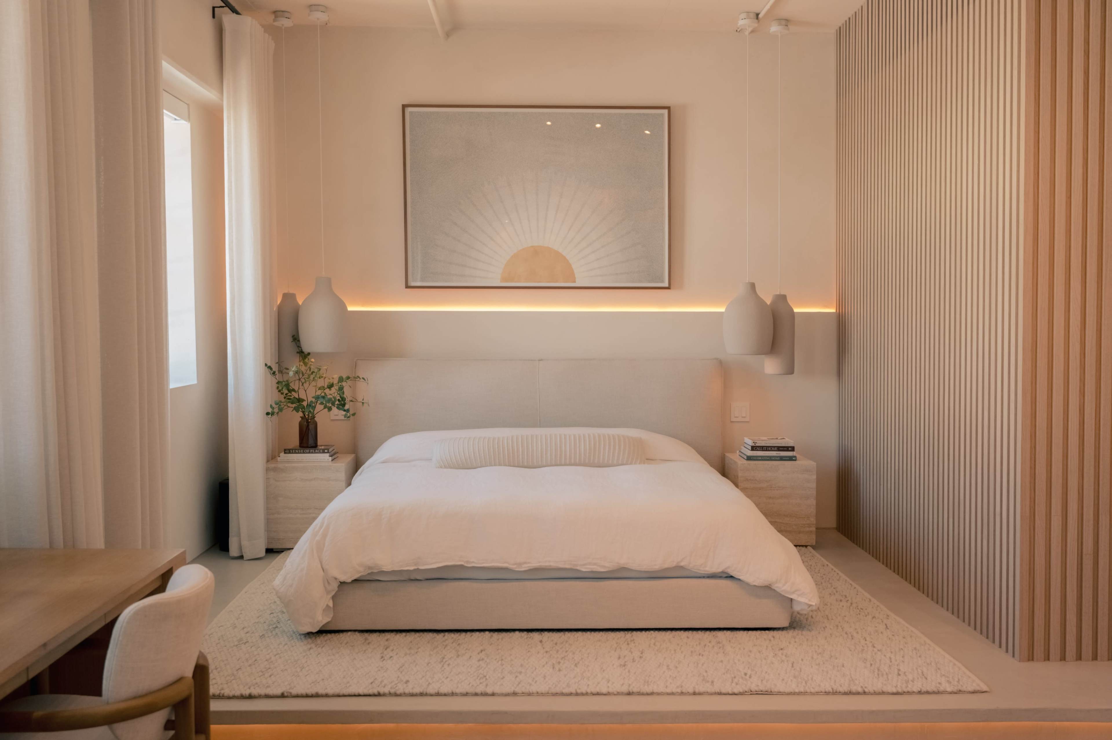 The image shows a modern bedroom with a large bed, minimalist furnishings, and soft lighting.