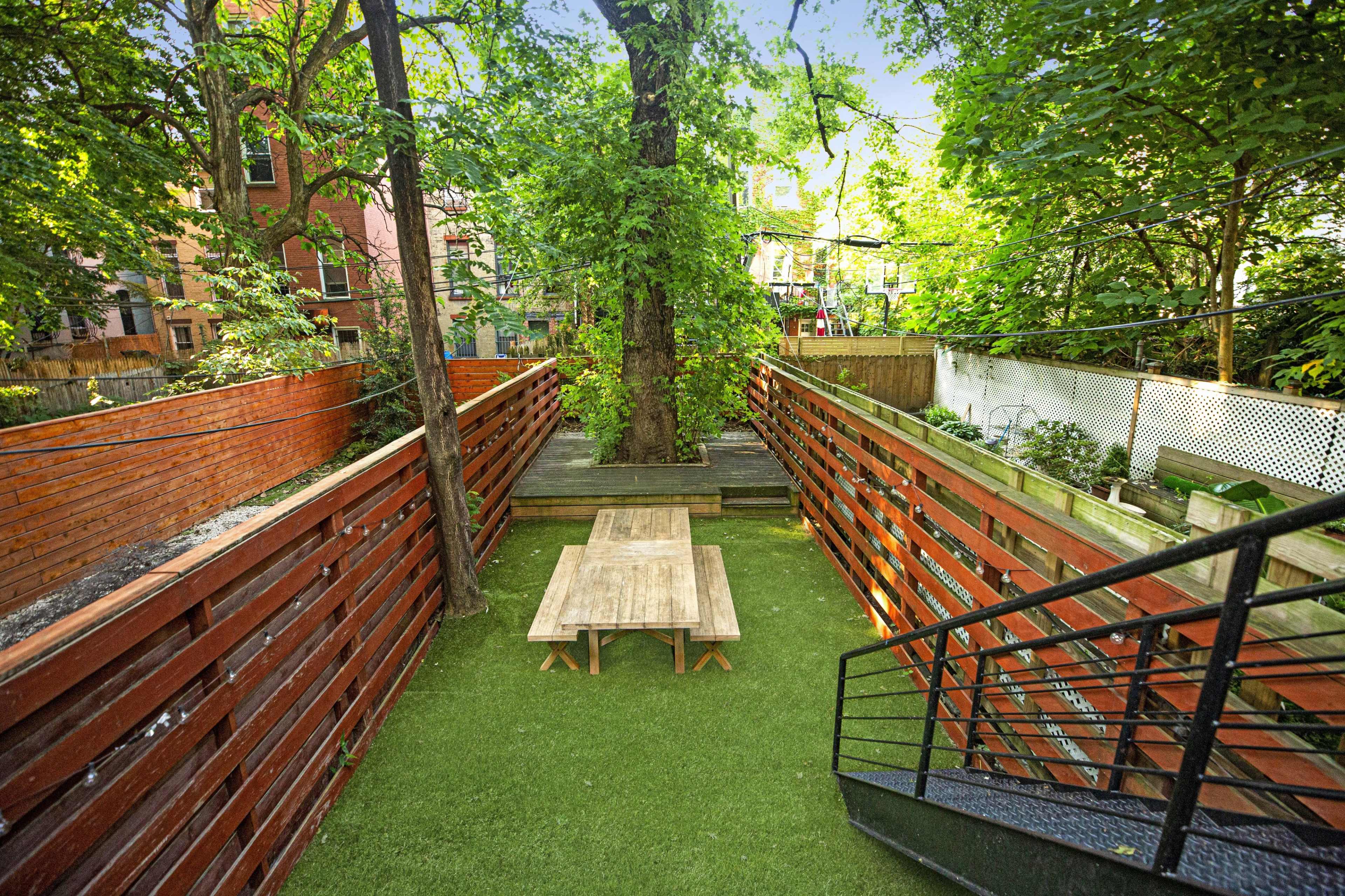 A small outdoor space with wooden fencing, a central tree, a table, and artificial grass.