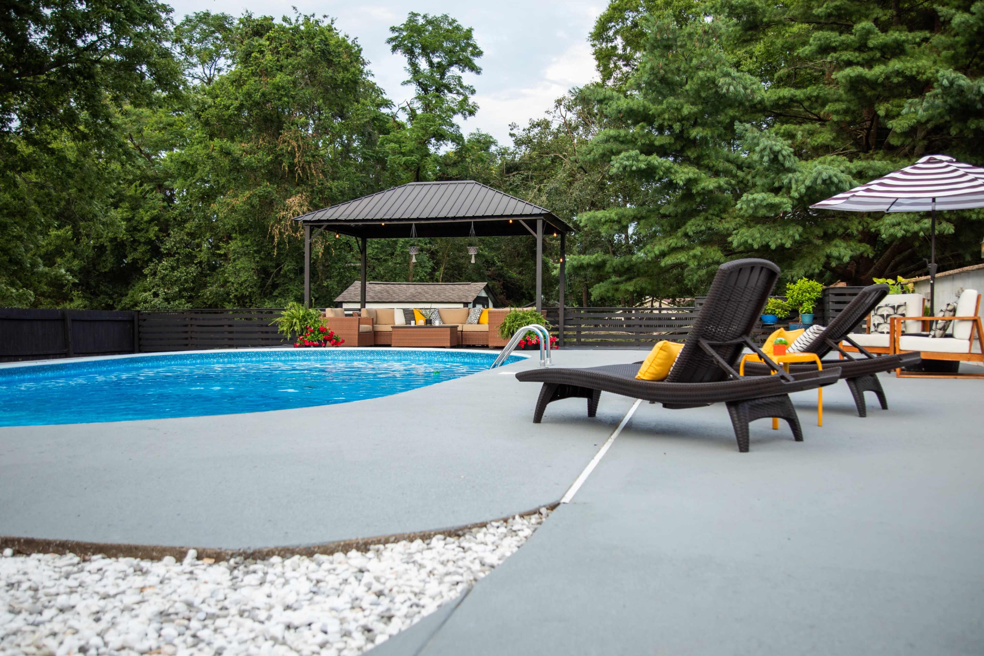 A landscaped pool area featuring a blue swimming pool, lounge chairs, and a gazebo surrounded by greenery.
