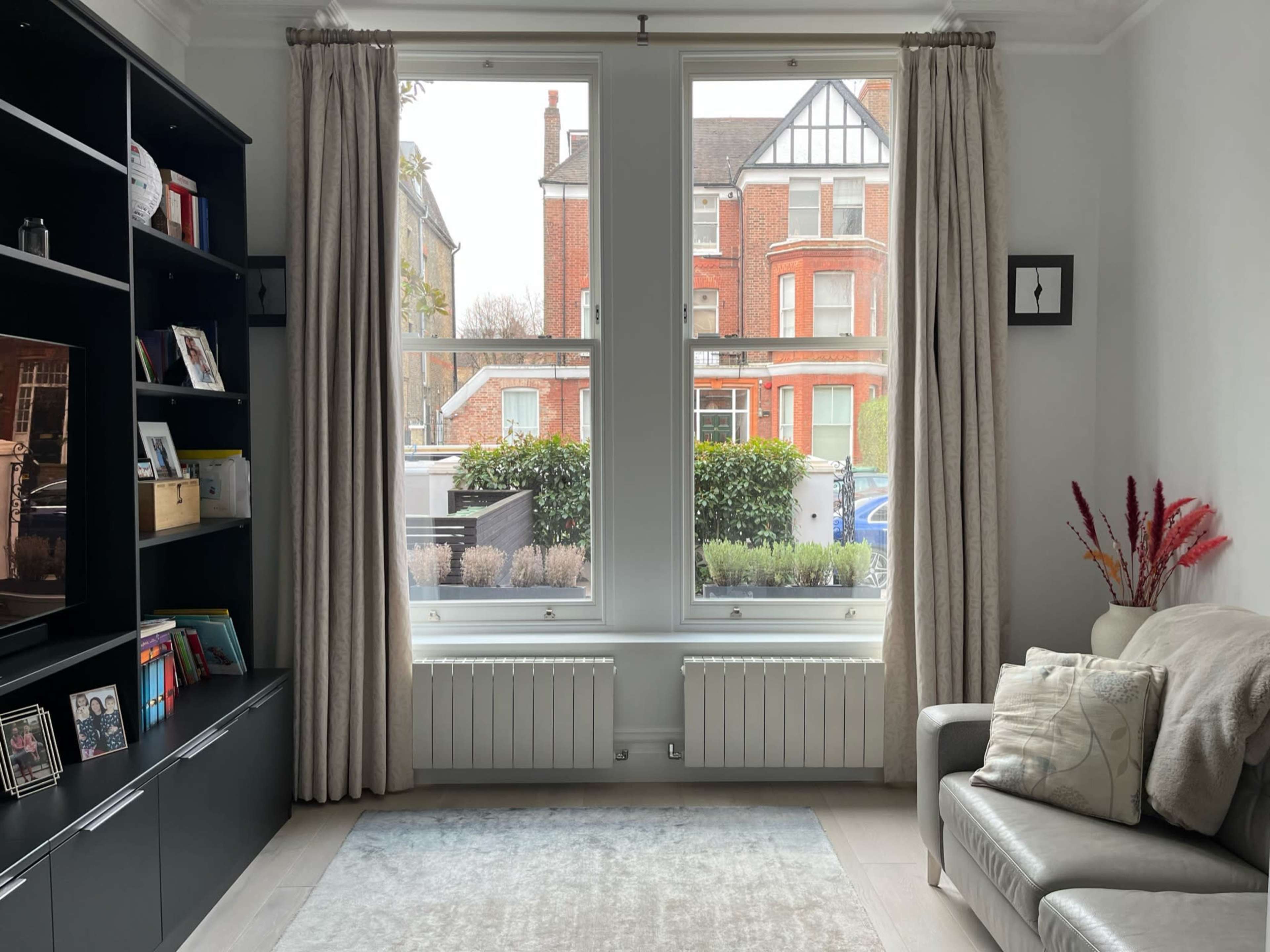 A living room features a sofa and bookshelf, with large windows overlooking a brick townhouse and garden.