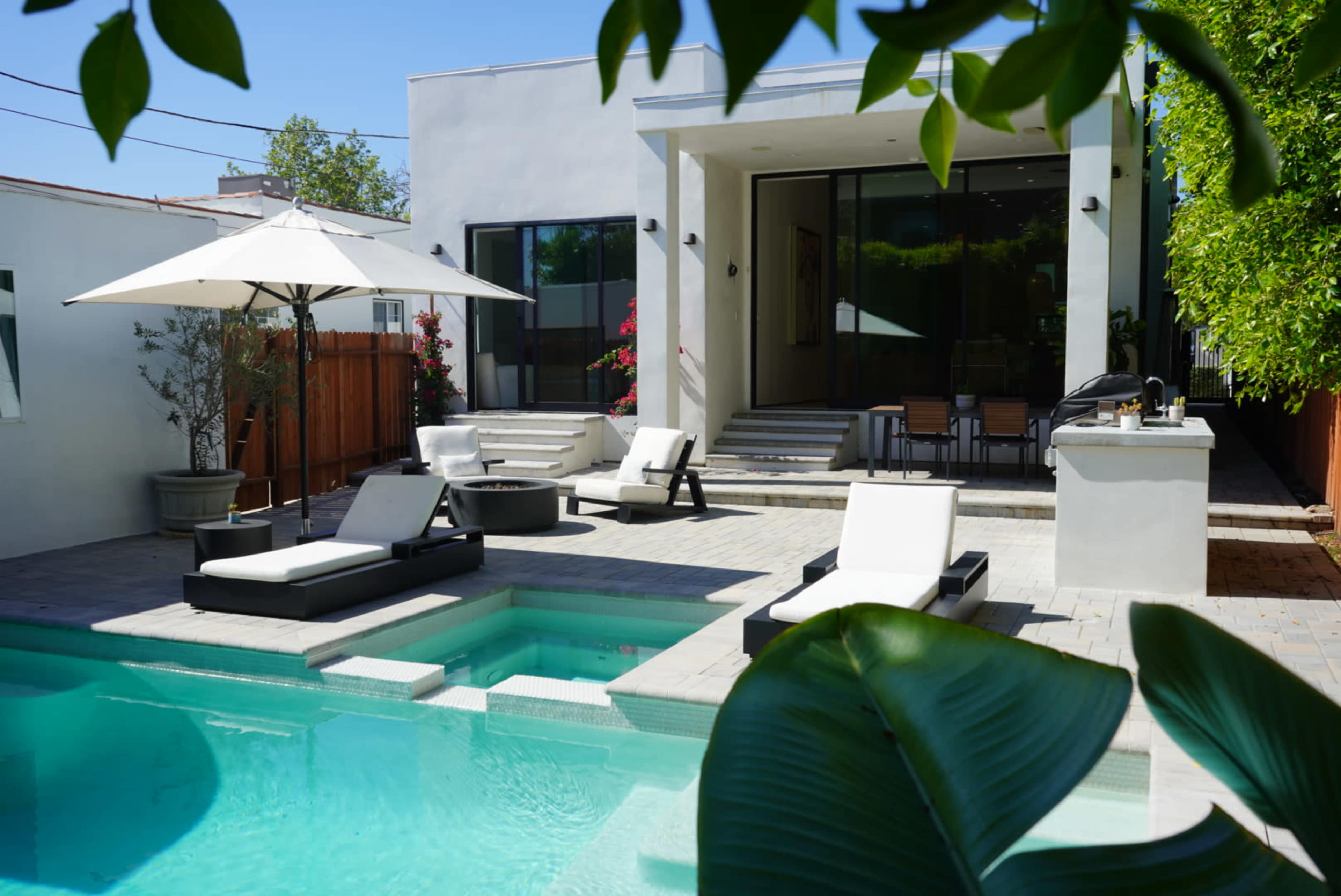 The image shows a modern backyard with a swimming pool, lounge chairs, and a patio area adjacent to a contemporary house.