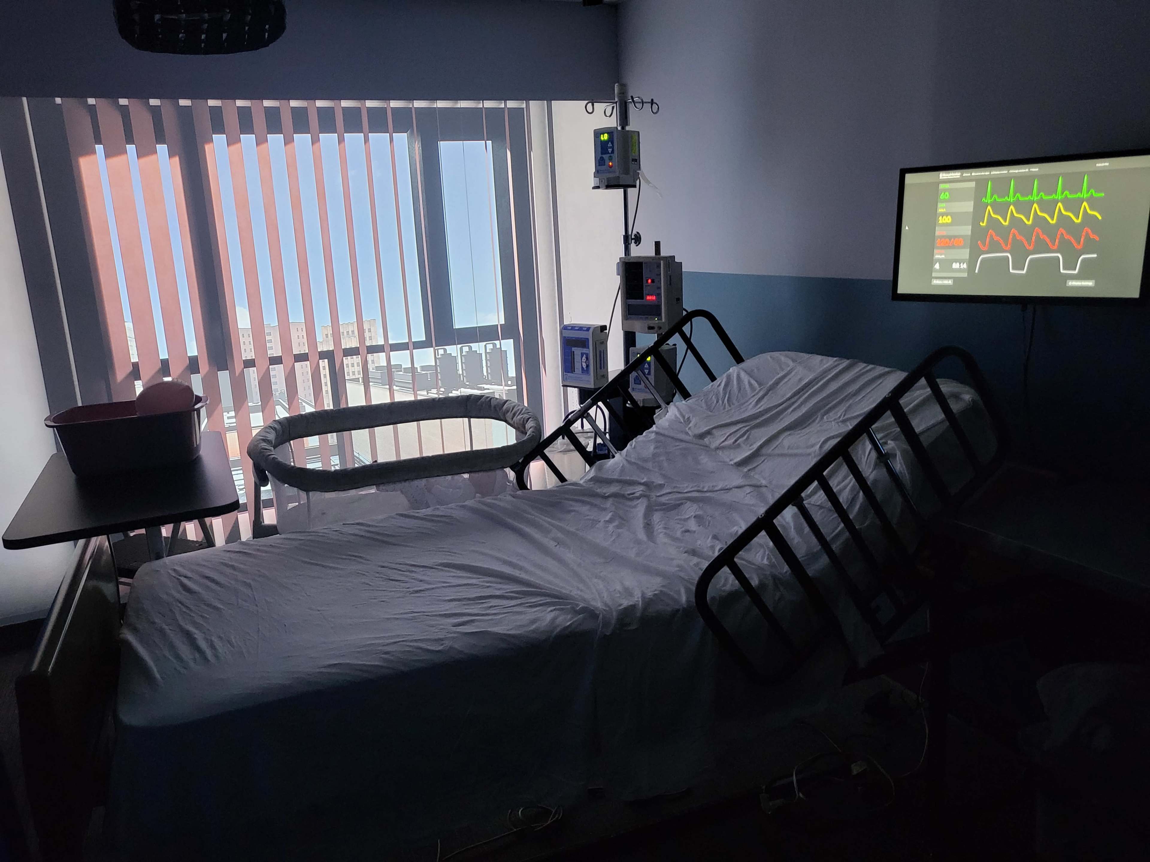 The image shows a hospital room with a bed, medical equipment, and a window covered by blinds.