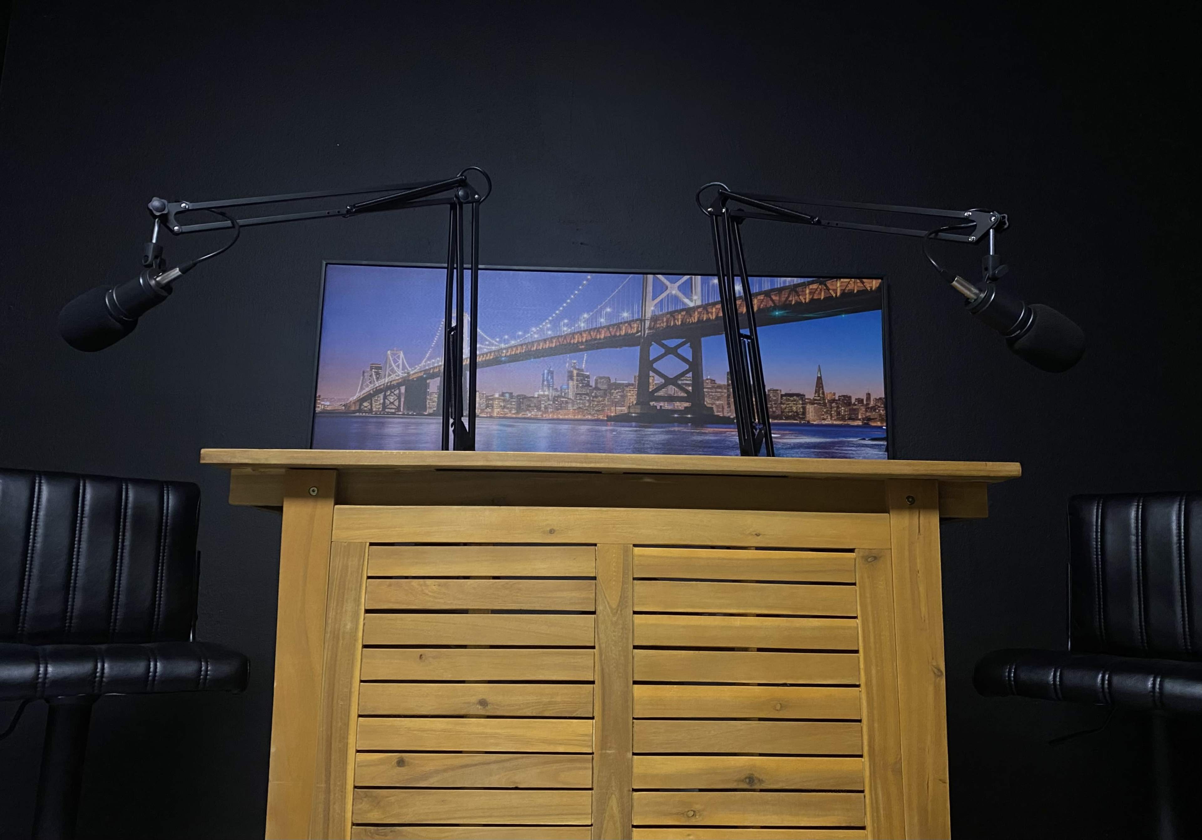 A wooden podium with two microphones and a backdrop image of a bridge against a dark wall.