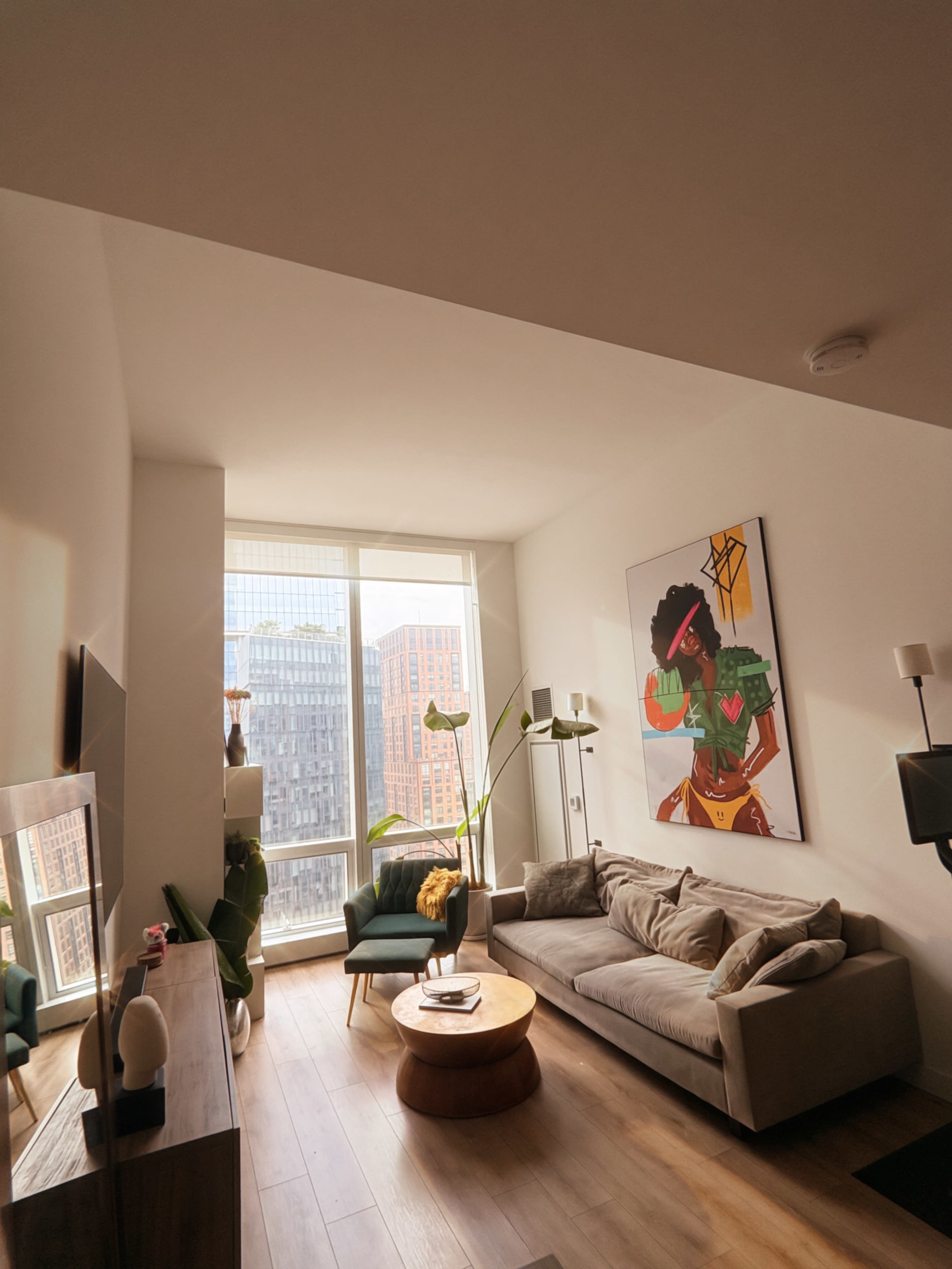A modern living room features a large window overlooking a cityscape, with a comfortable sofa, a coffee table, and a vibrant piece of artwork on the wall.