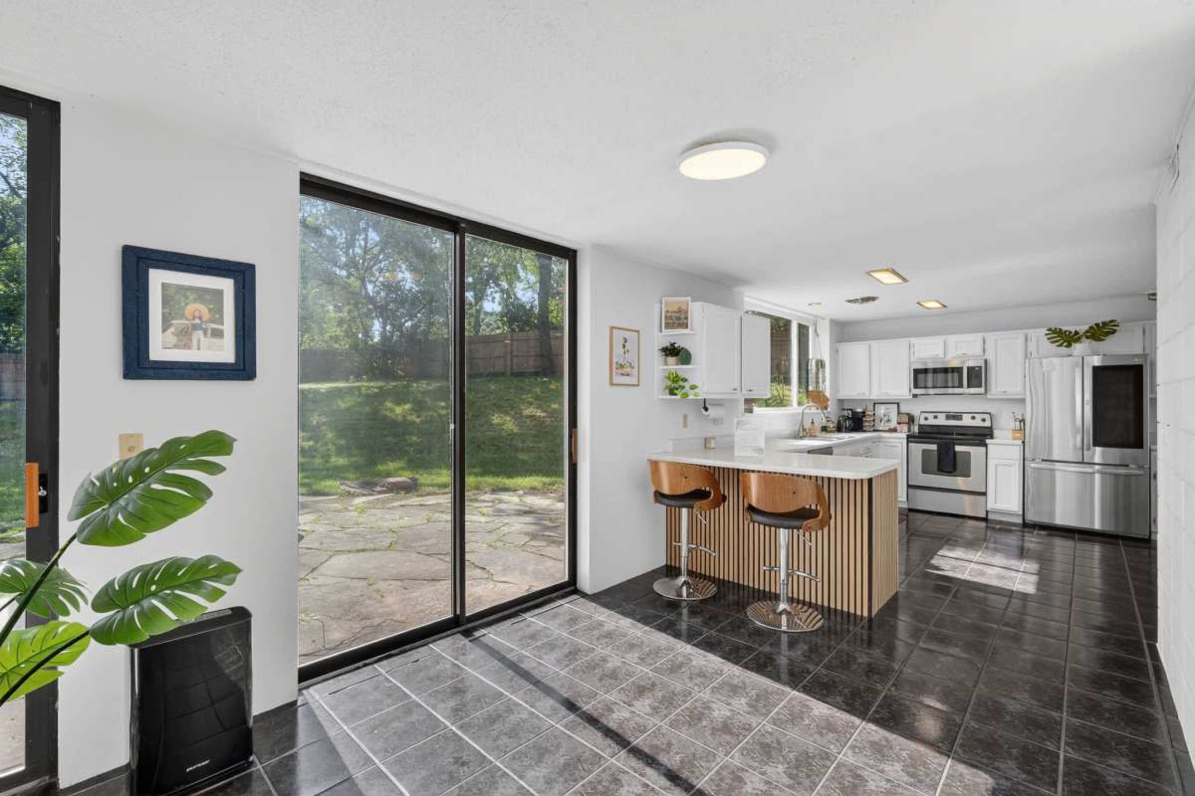 The image shows a modern kitchen with a breakfast bar, large windows, and a view of a backyard.