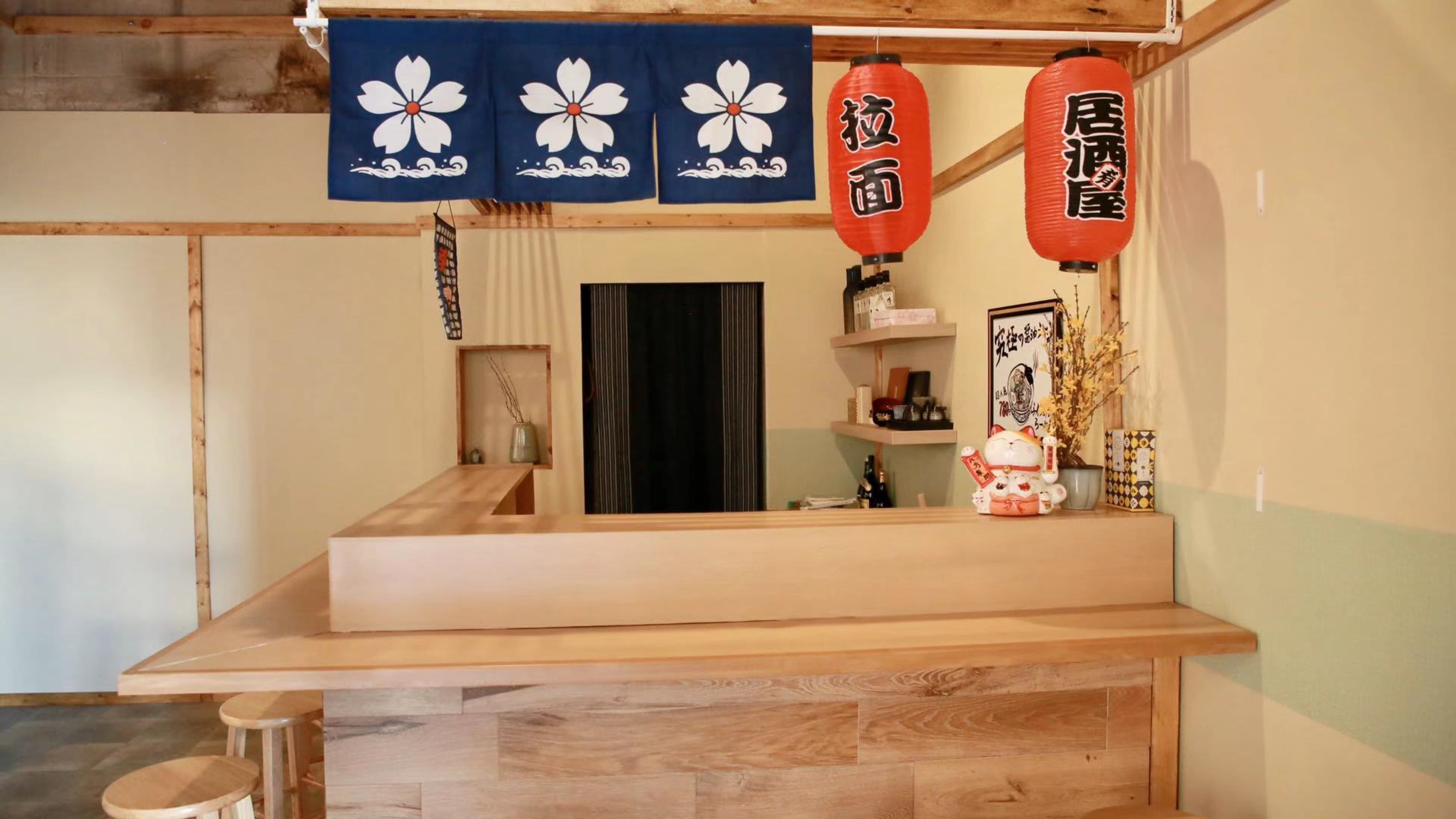 The image shows a wooden bar area with a dark curtain in the background, adorned with decorative lanterns and a traditional blue fabric banner.